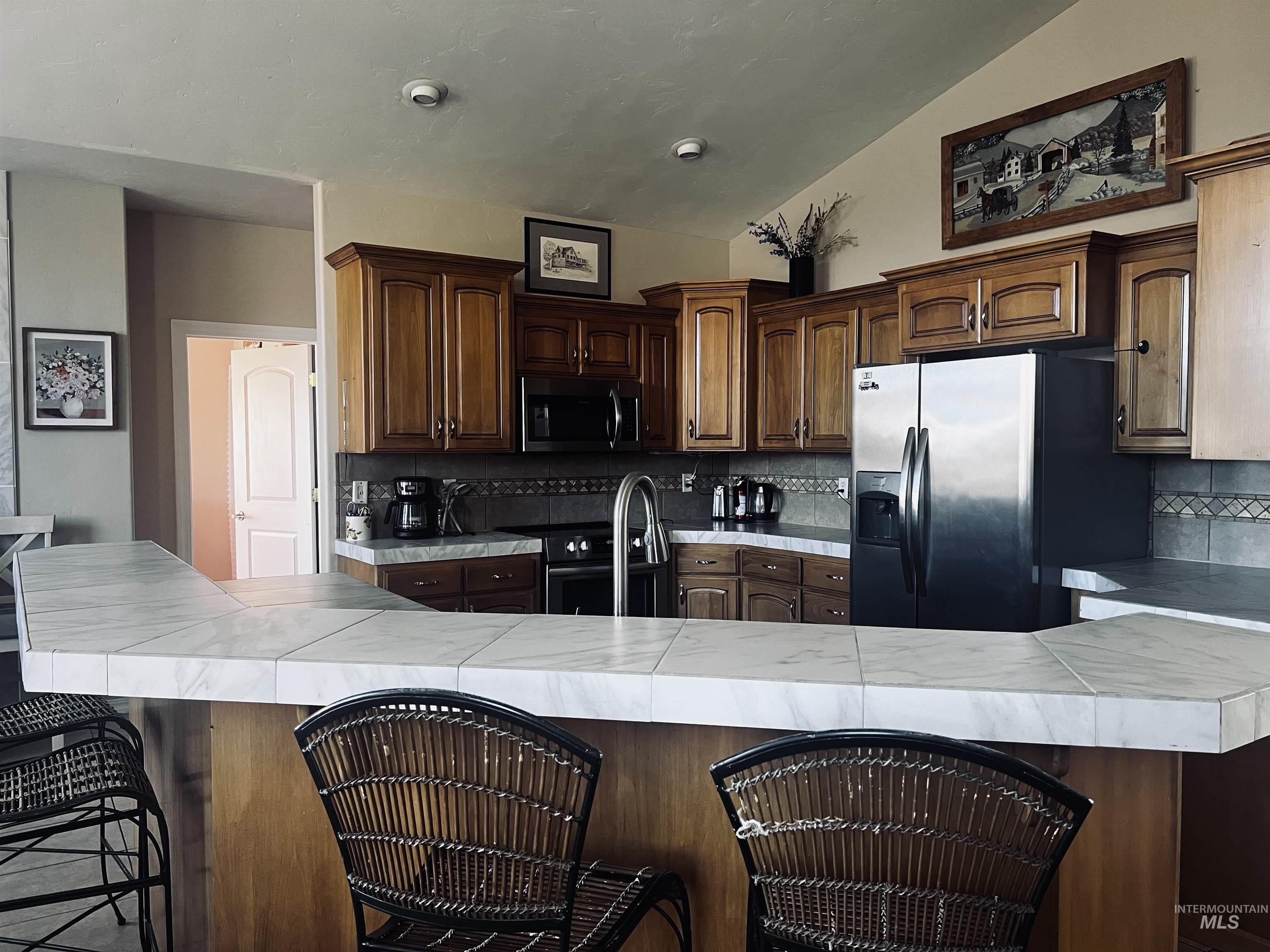 Kitchen featuring a breakfast bar, tile countertops, stainless steel appliances, lofted ceiling, and backsplash