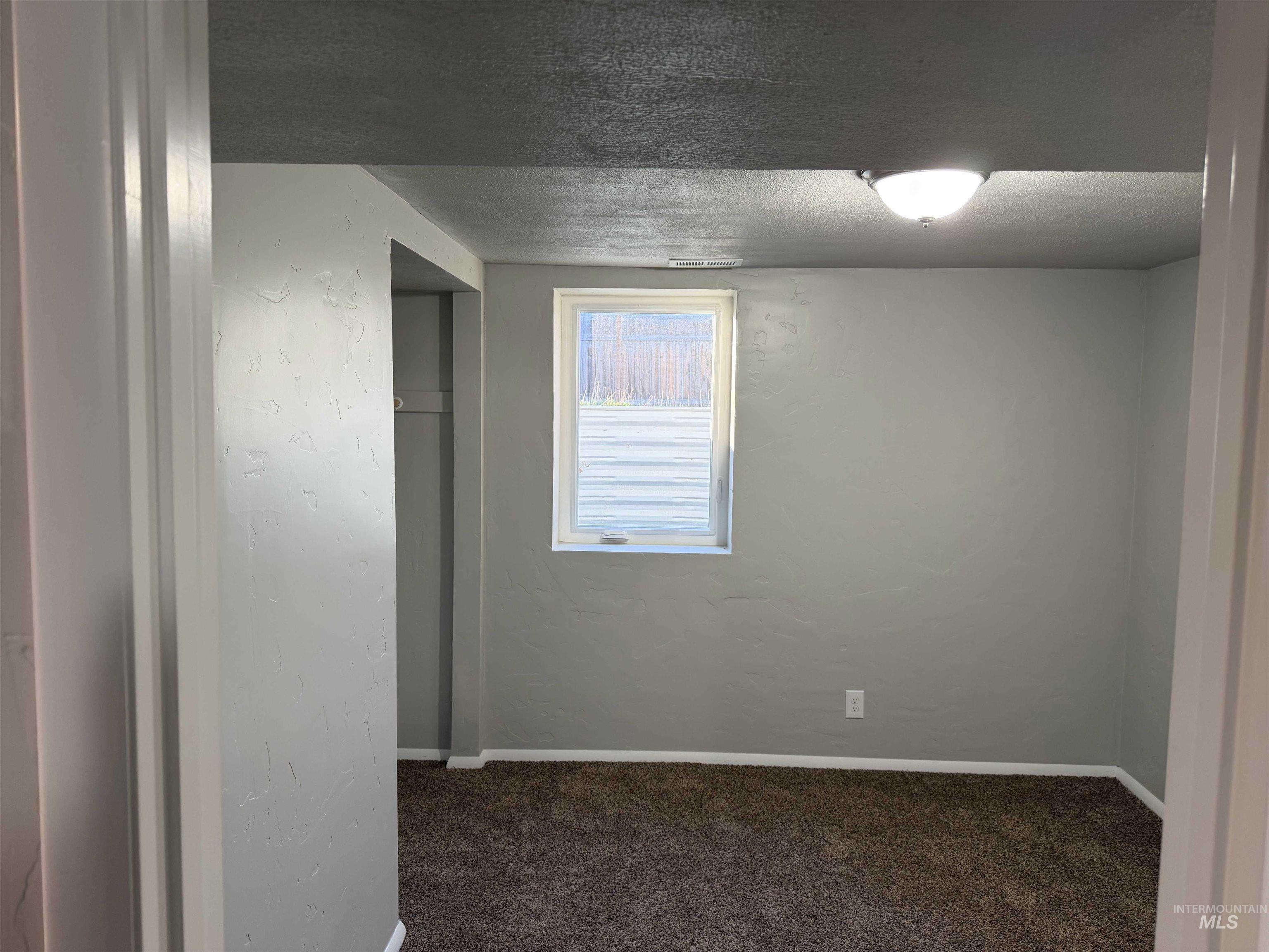 Unfurnished room with a textured ceiling, dark colored carpet, and a textured wall