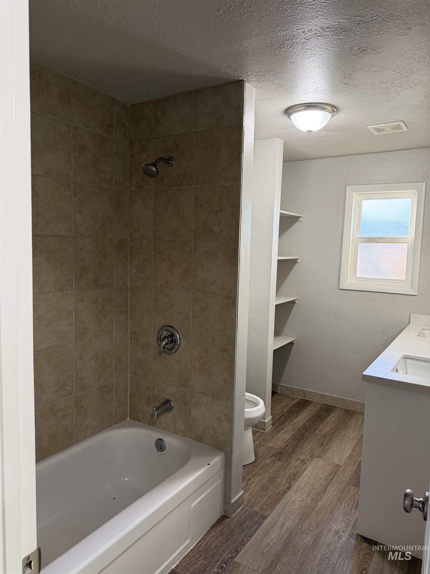 Full bathroom with a textured ceiling, bathing tub / shower combination, double vanity, and dark wood finished floors