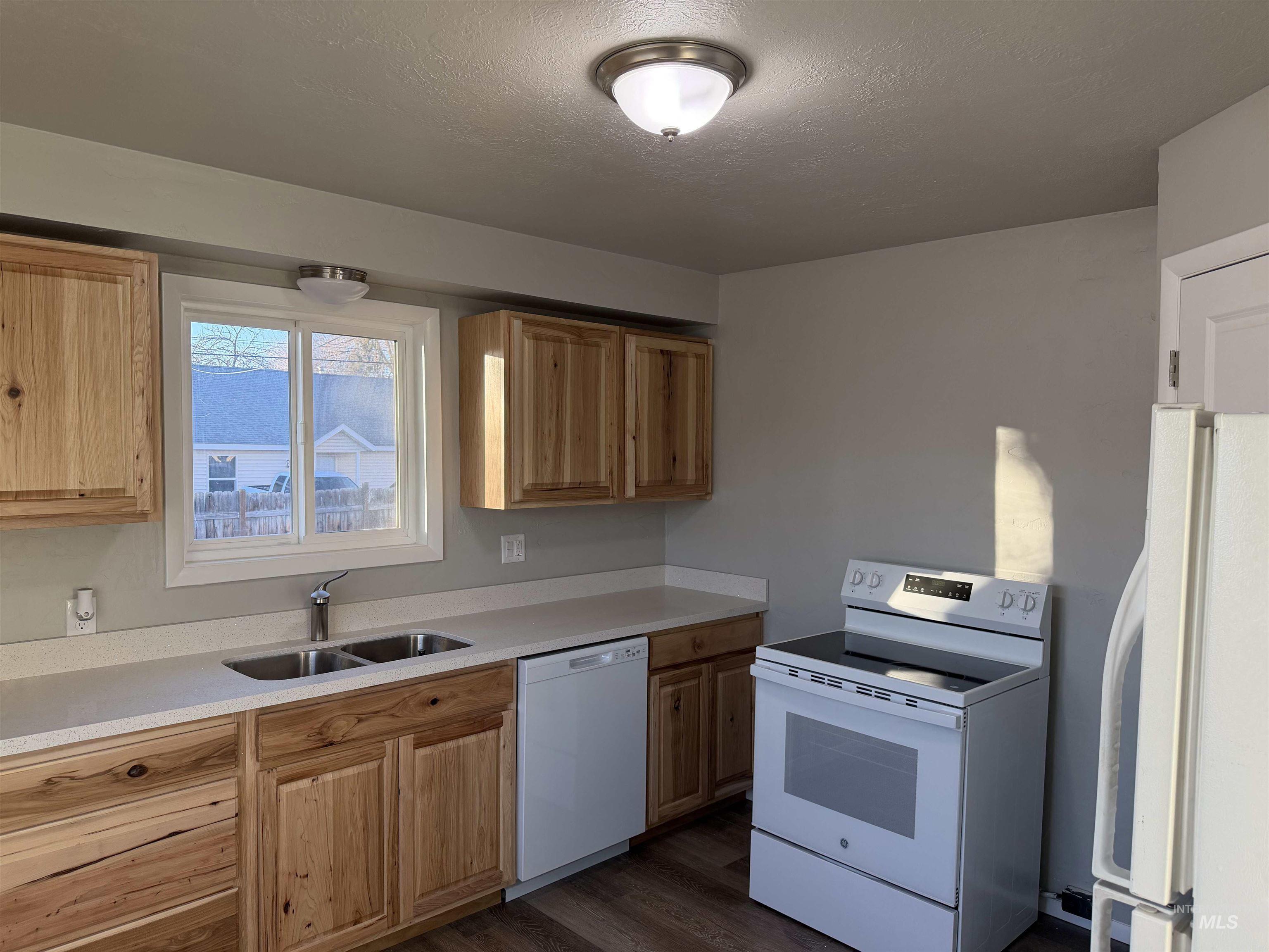 Kitchen with white appliances, a textured ceiling, dark wood finished floors, light brown cabinets, and light stone counters