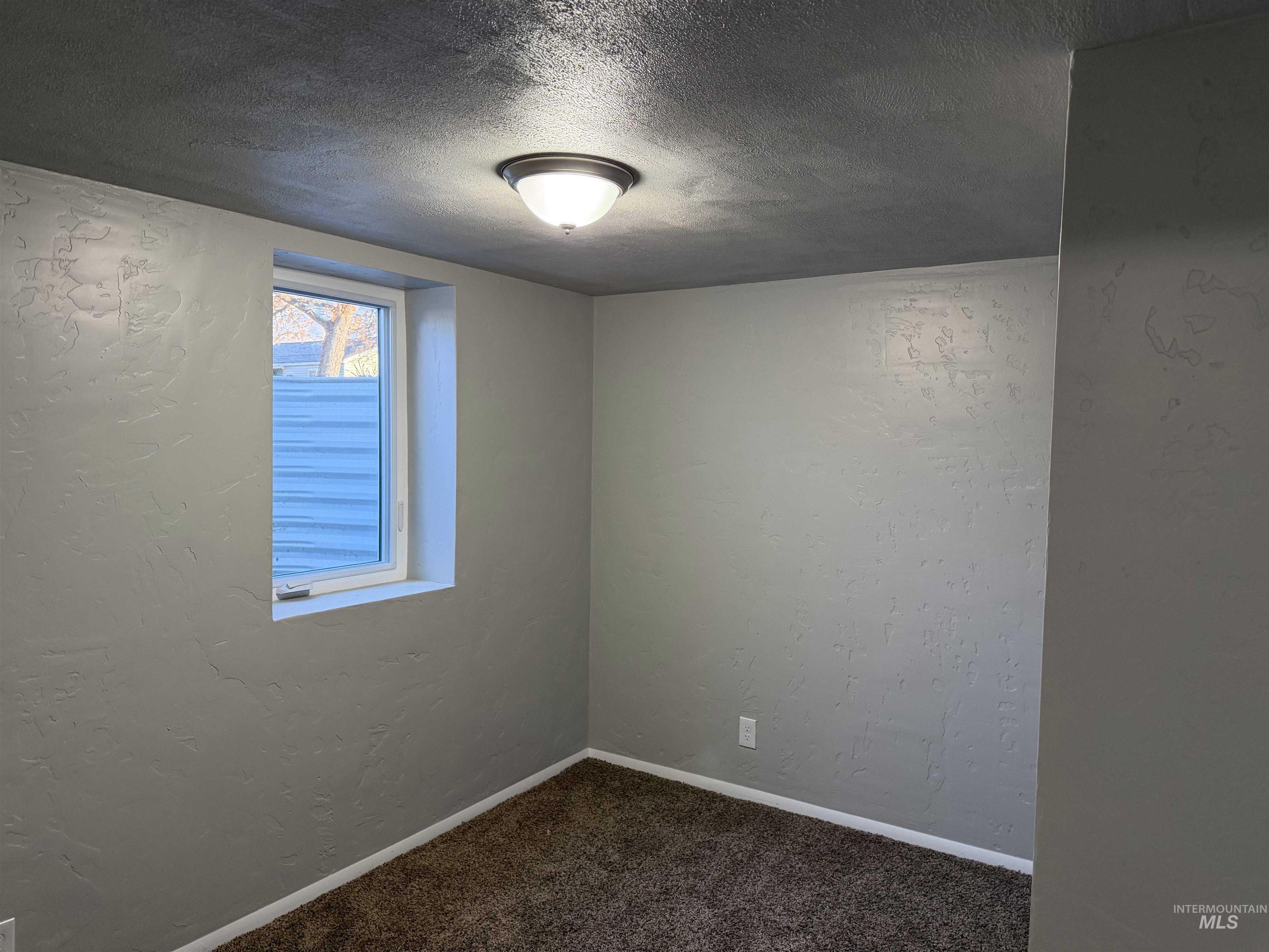 Unfurnished room featuring a textured wall, a textured ceiling, and dark colored carpet