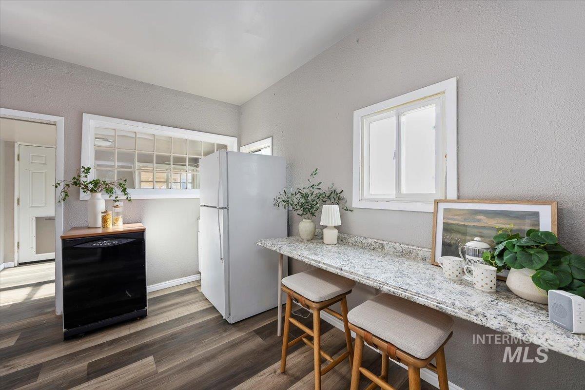 Kitchen with a textured wall, freestanding refrigerator, dishwasher, dark wood finished floors, and a kitchen breakfast bar