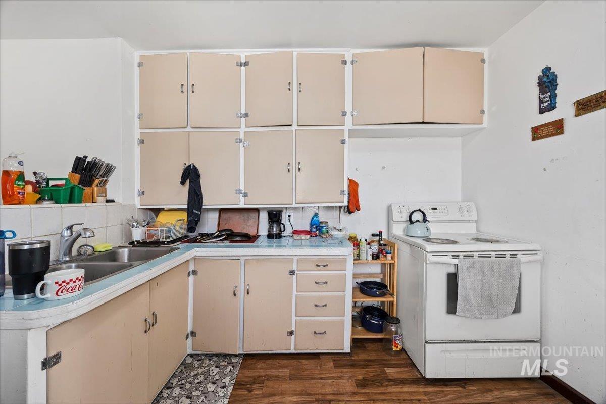 Kitchen featuring white electric range, light countertops, dark wood-type flooring, cream cabinets, and backsplash