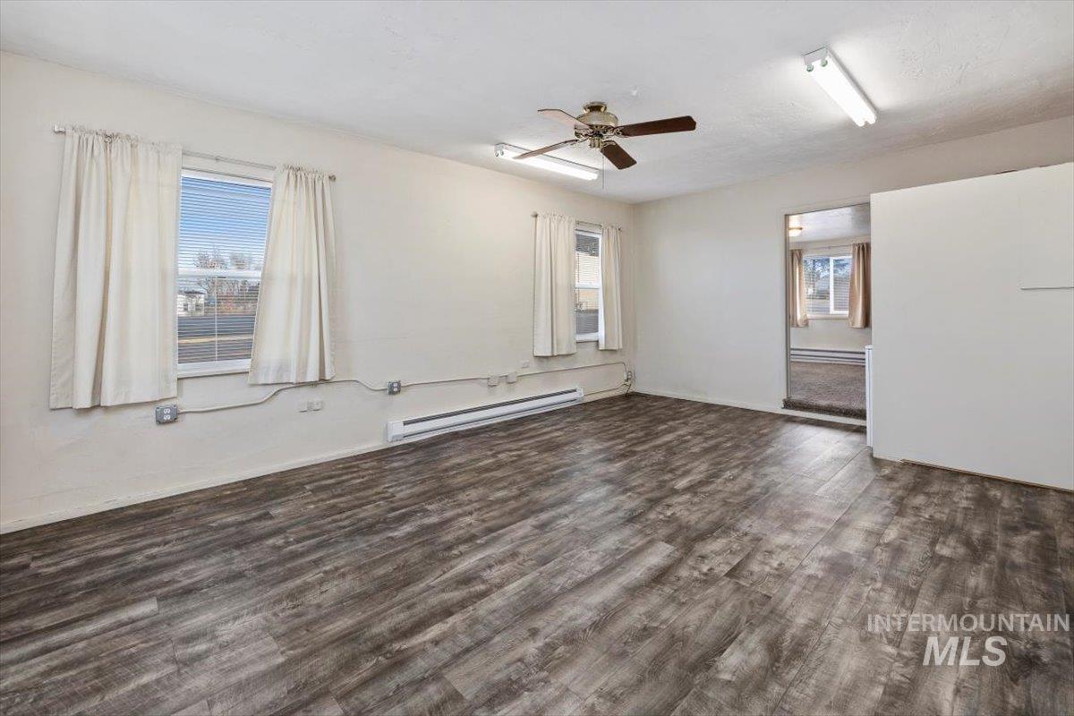 Empty room featuring a baseboard radiator, dark wood-style flooring, plenty of natural light, and a ceiling fan