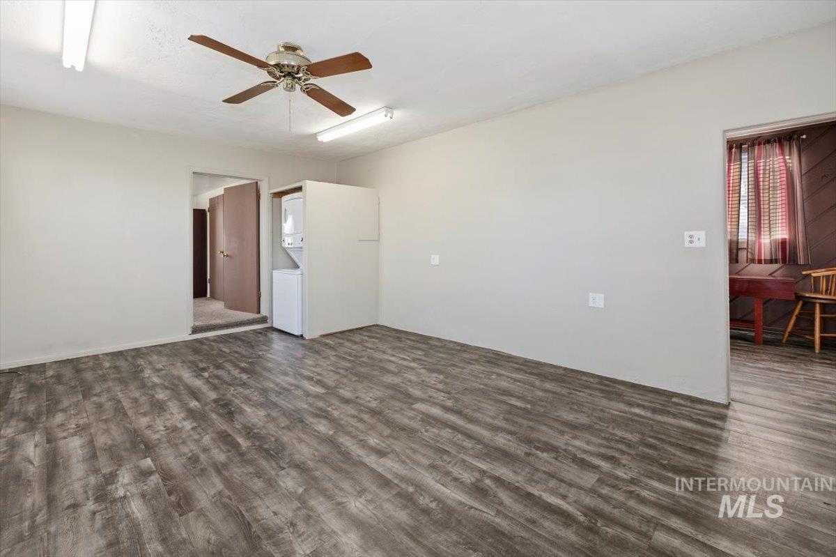 Unfurnished room featuring dark wood finished floors, stacked washer and clothes dryer, and ceiling fan