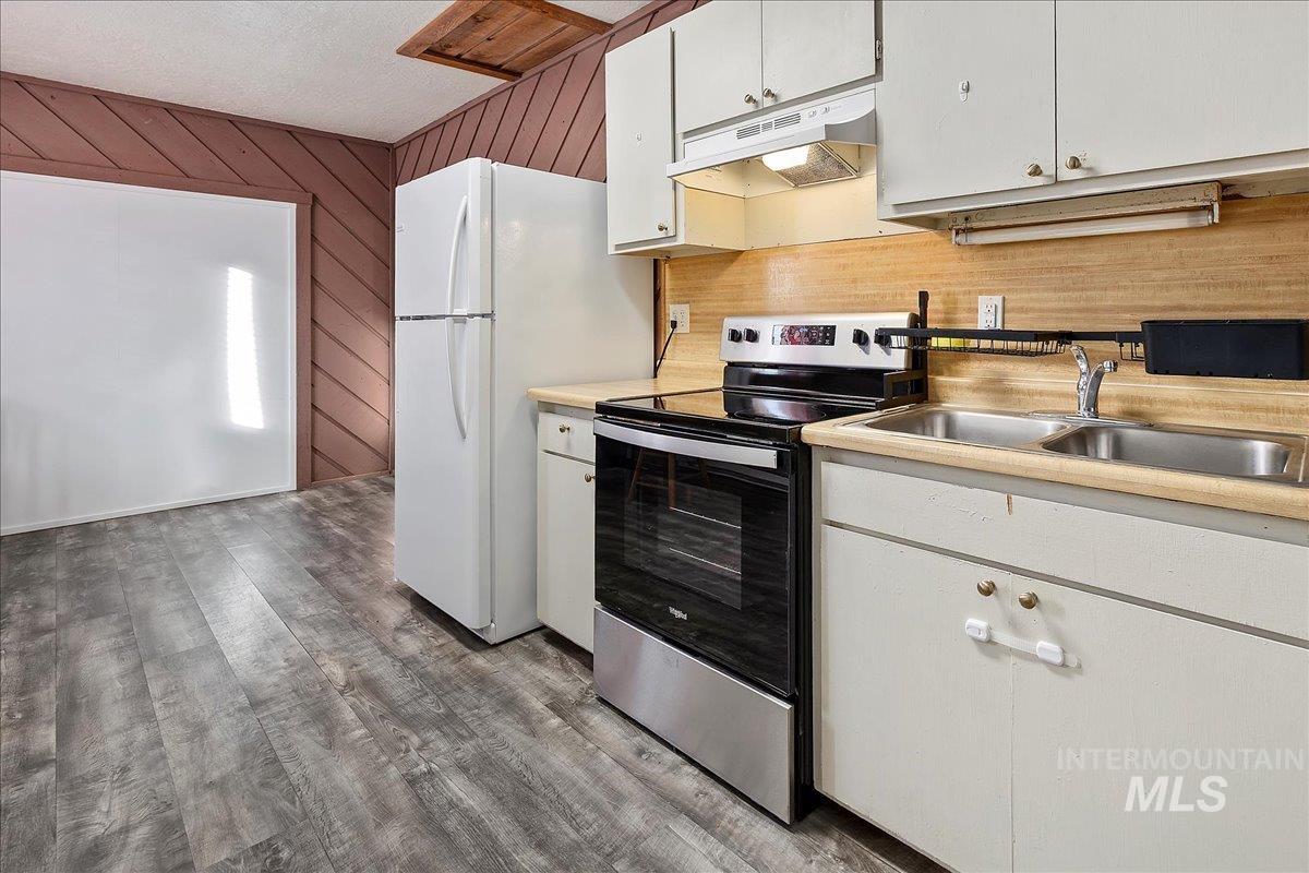 Kitchen with electric stove, wood walls, light countertops, white cabinetry, and under cabinet range hood