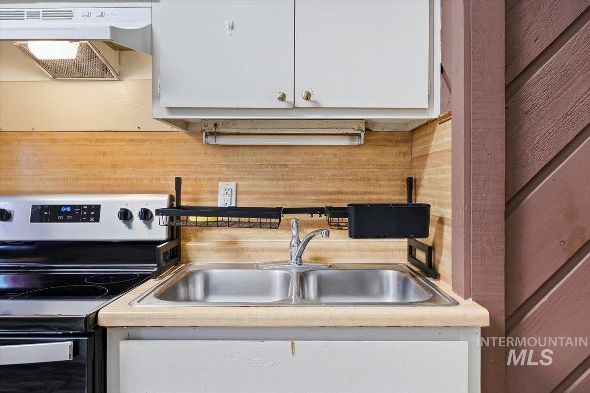 Kitchen featuring stainless steel range with electric stovetop, exhaust hood, light countertops, and white cabinets
