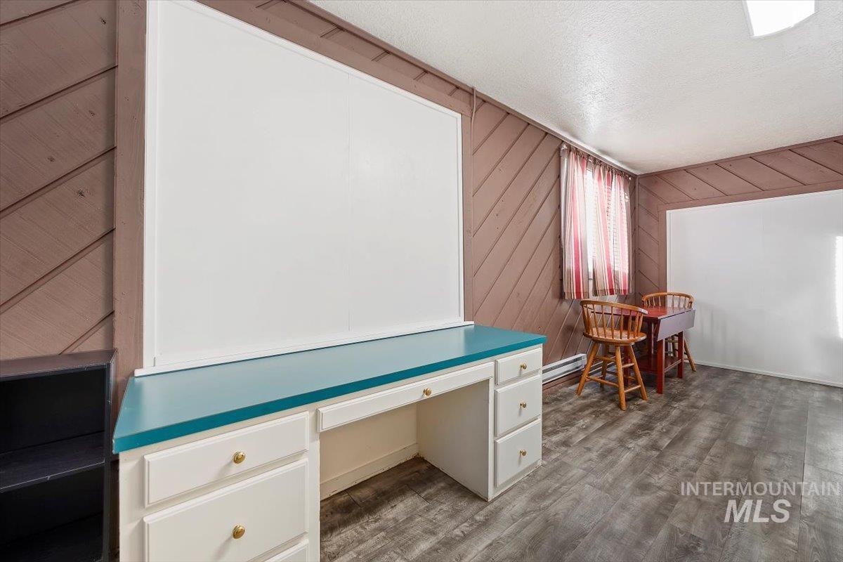 Office space featuring wood walls, a textured ceiling, dark wood-style flooring, built in desk, and a baseboard heating unit