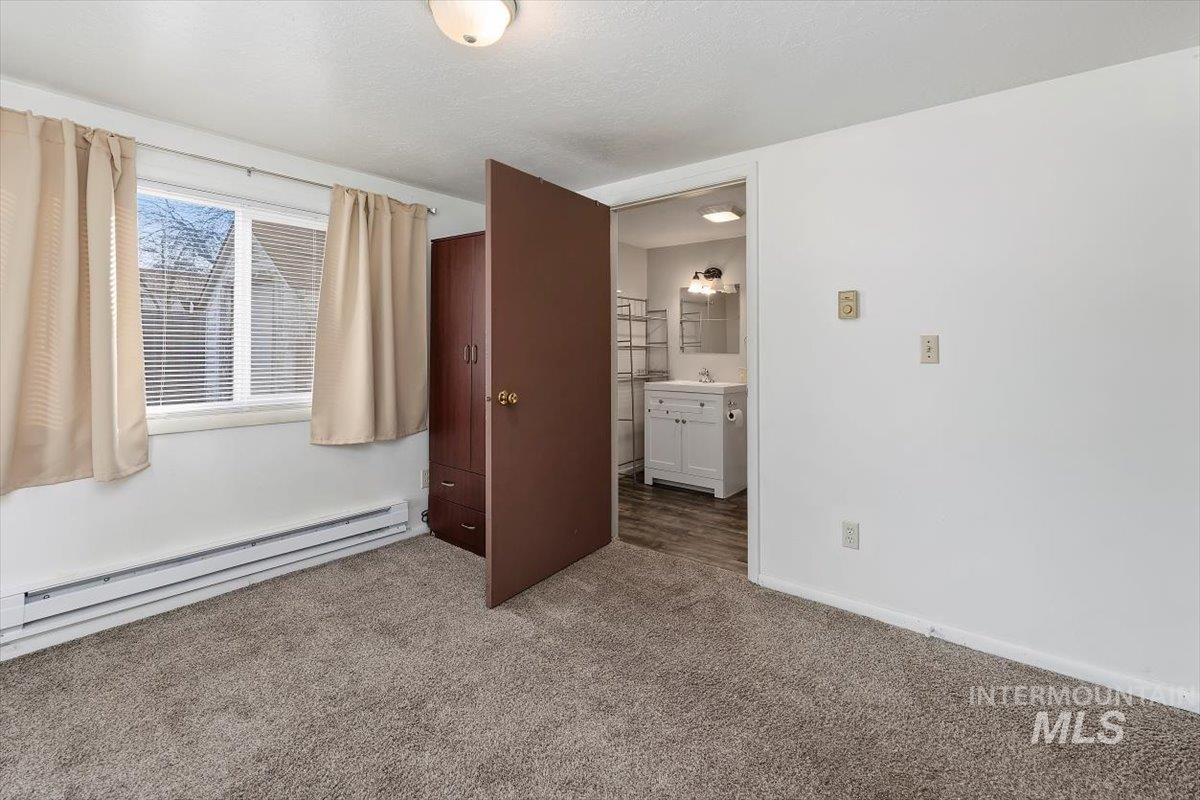 Unfurnished bedroom with a baseboard radiator, connected bathroom, carpet floors, and a textured ceiling