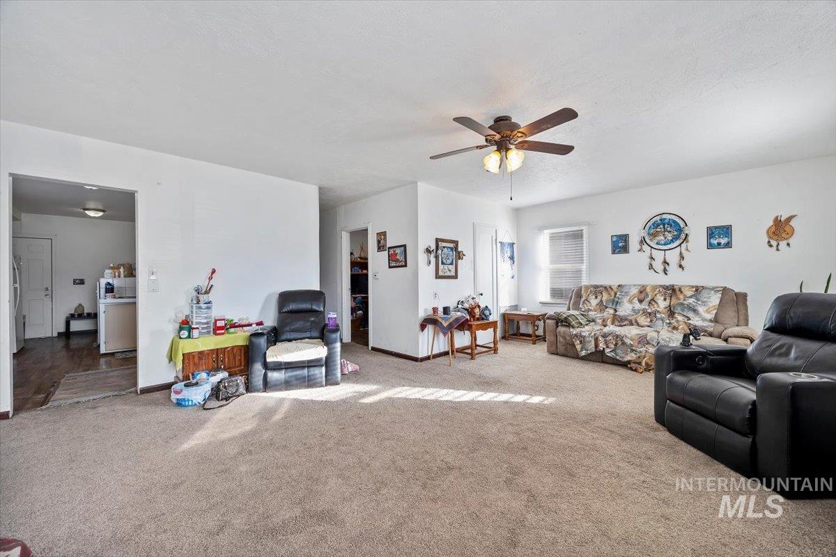 Carpeted living area with ceiling fan and baseboards