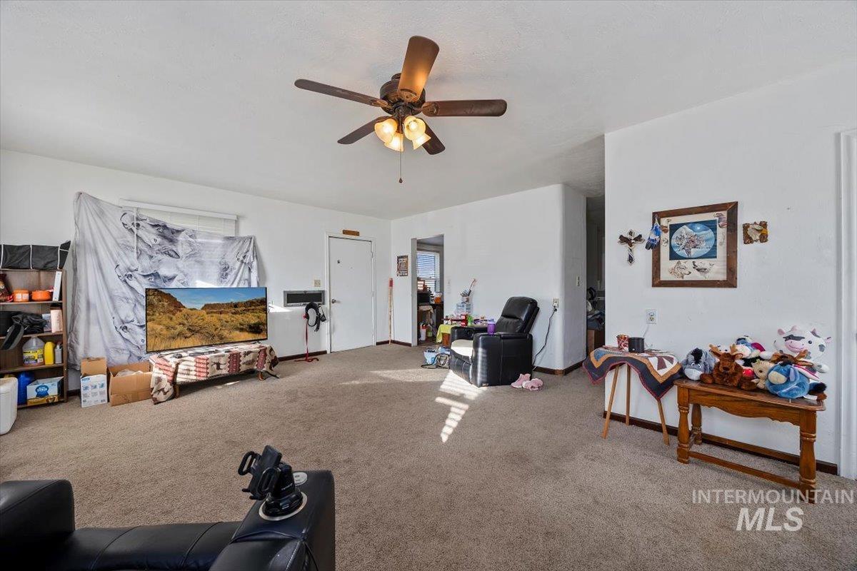 Carpeted living area featuring a ceiling fan and baseboards