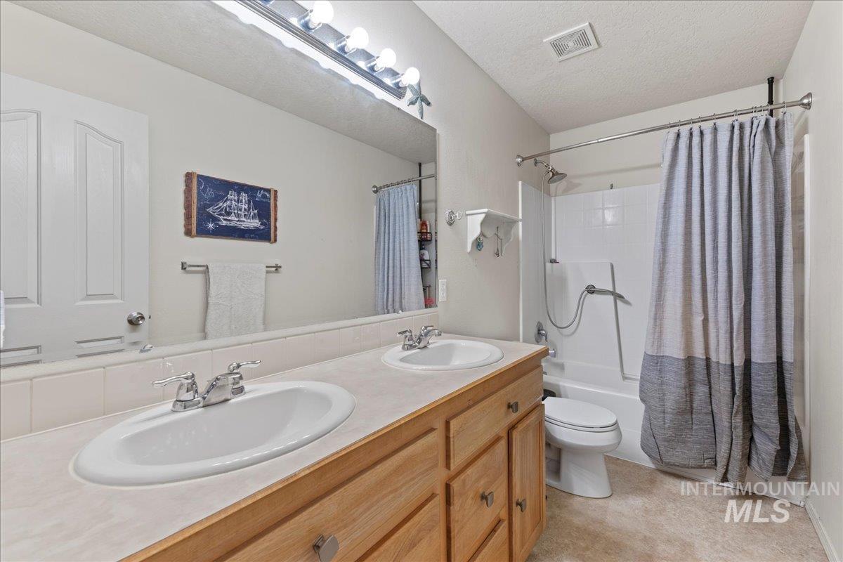 Bathroom featuring double vanity, shower / bathtub combination with curtain, and a textured ceiling