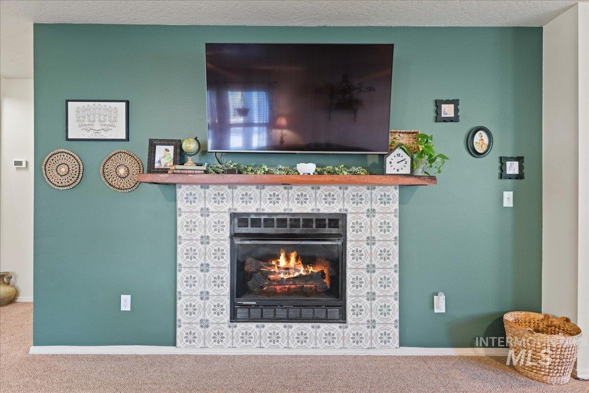 Detailed view of a tile fireplace, carpet flooring, and a textured ceiling