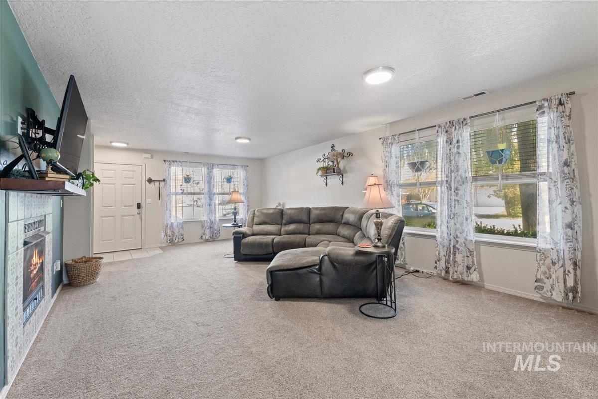 Living area featuring light carpet, a textured ceiling, and a tiled fireplace