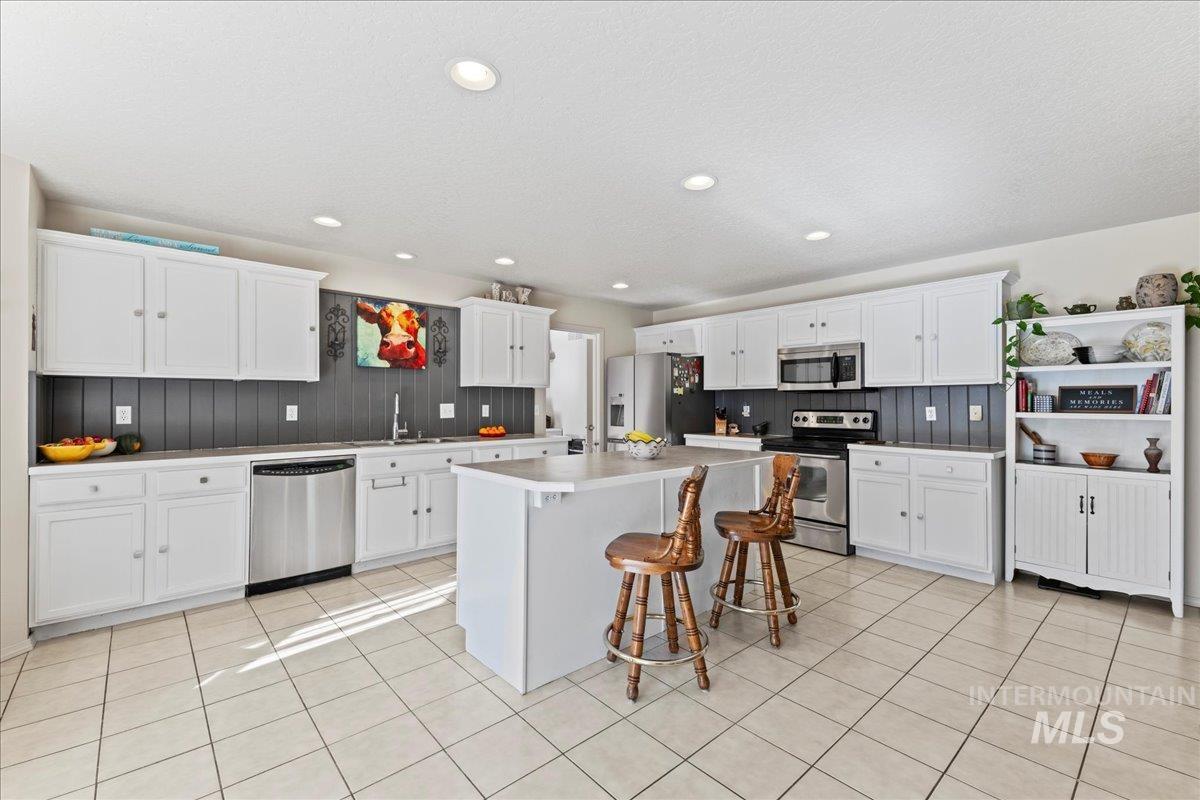 Kitchen with a kitchen bar, white cabinets, appliances with stainless steel finishes, a center island, and recessed lighting