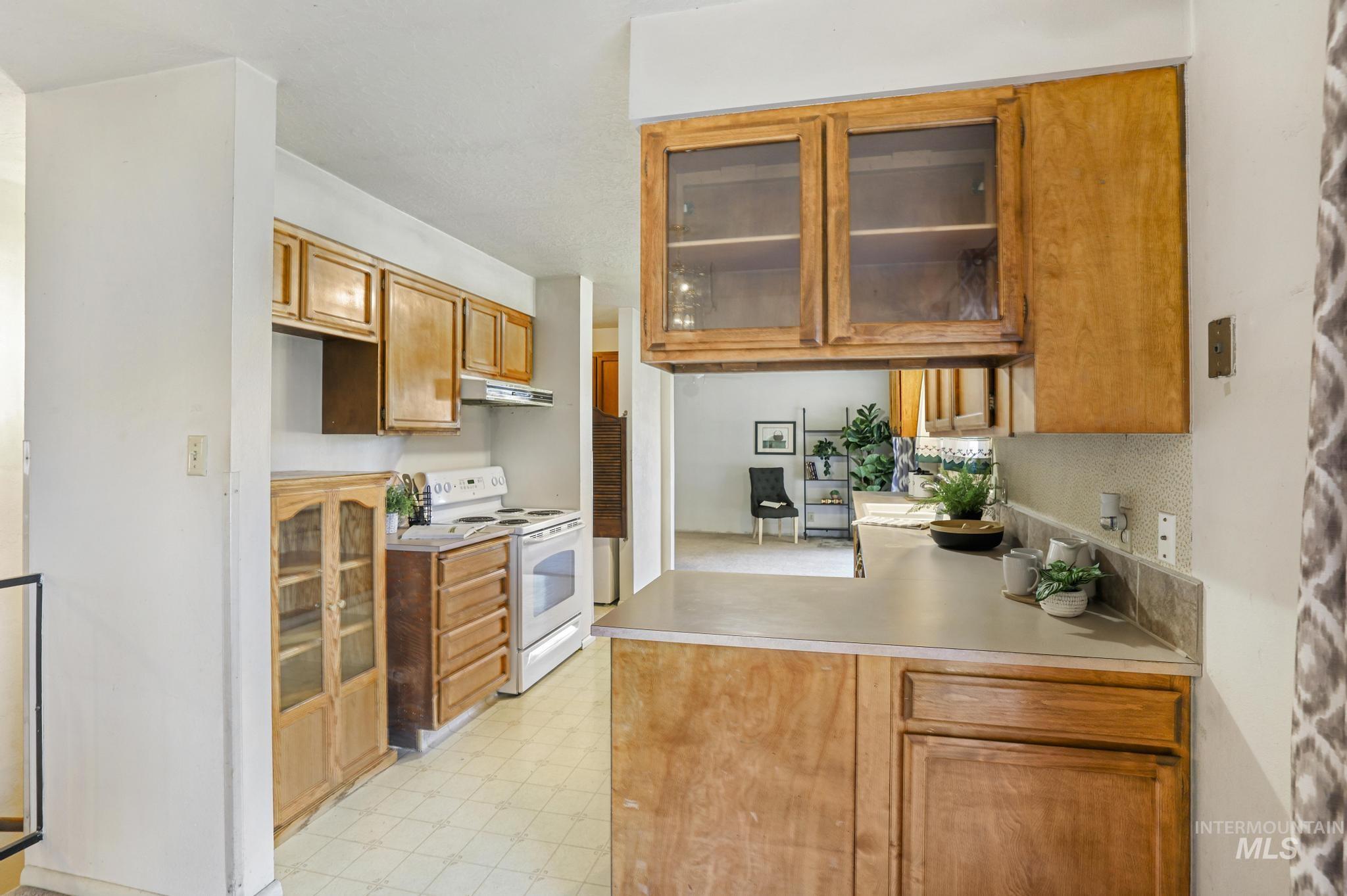 Kitchen featuring brown cabinets, light flooring, white electric range oven, light countertops, and a peninsula