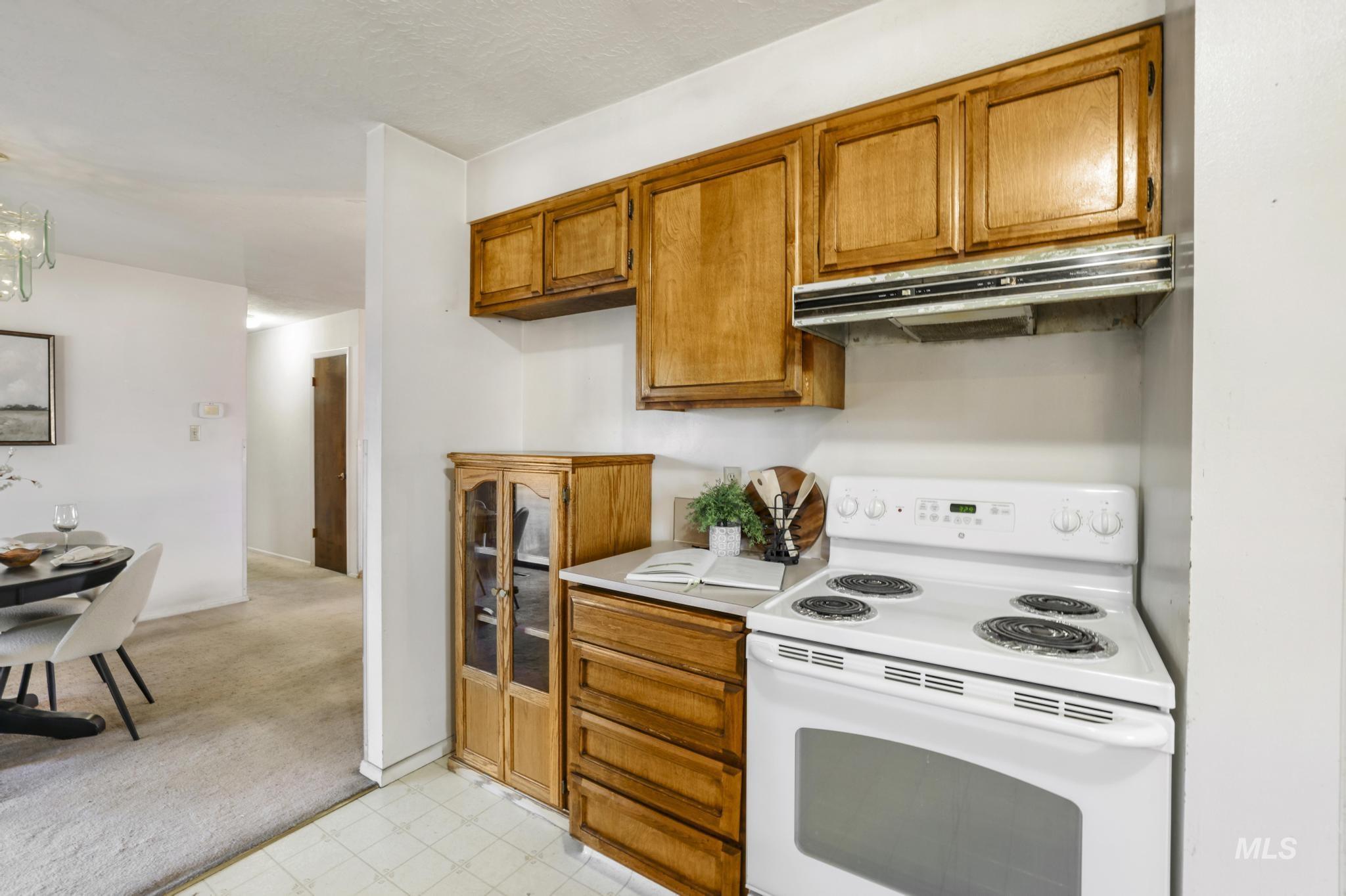 Kitchen featuring white electric range, brown cabinetry, light flooring, under cabinet range hood, and light colored carpet