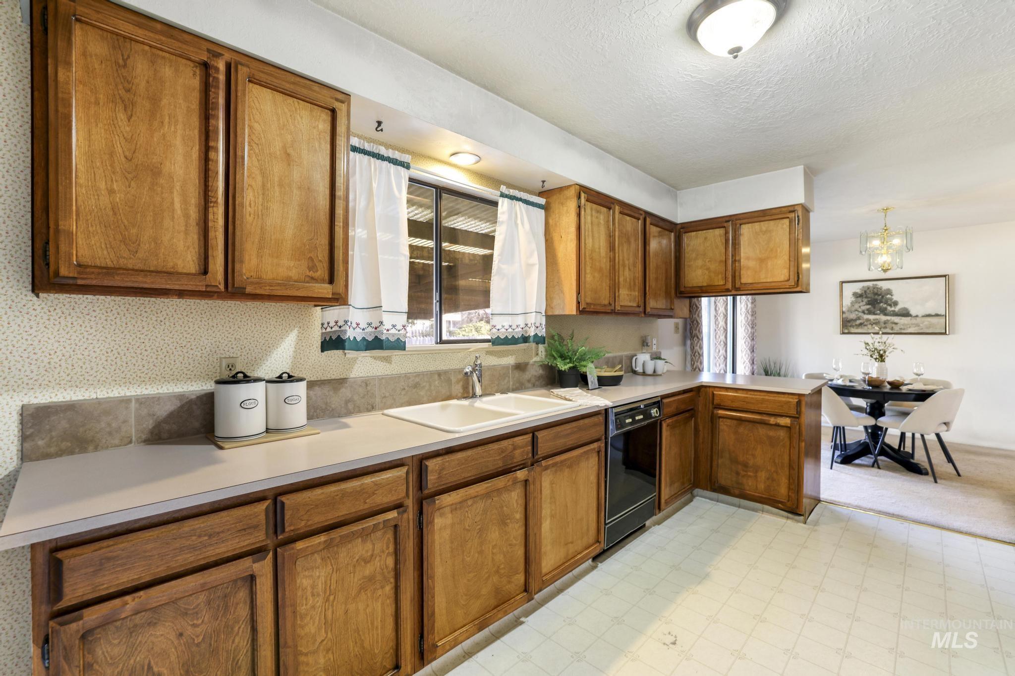 Kitchen with brown cabinets, light flooring, a peninsula, light countertops, and a chandelier