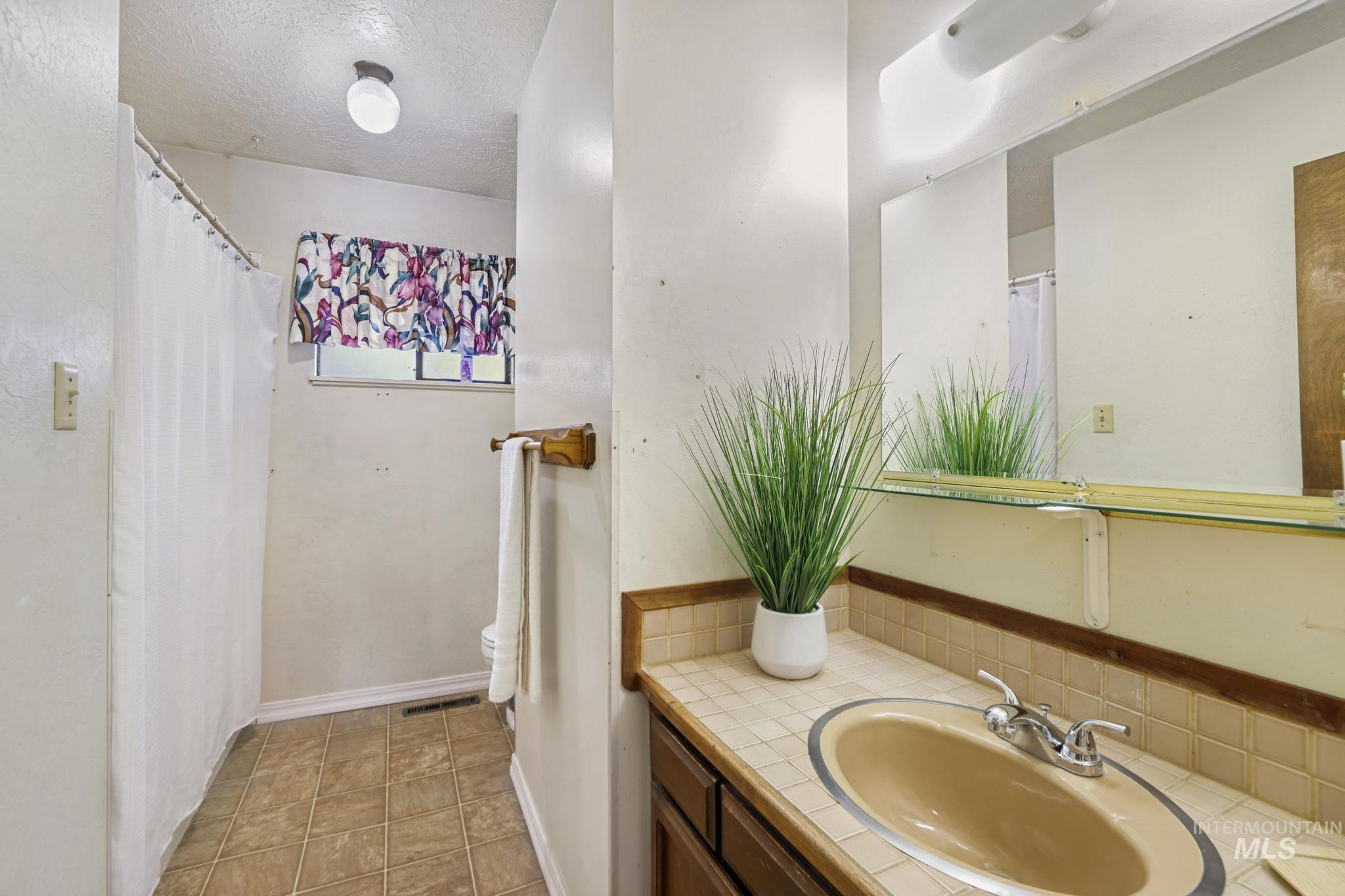 Full bathroom with a textured ceiling, vanity, a shower with shower curtain, and light tile patterned flooring