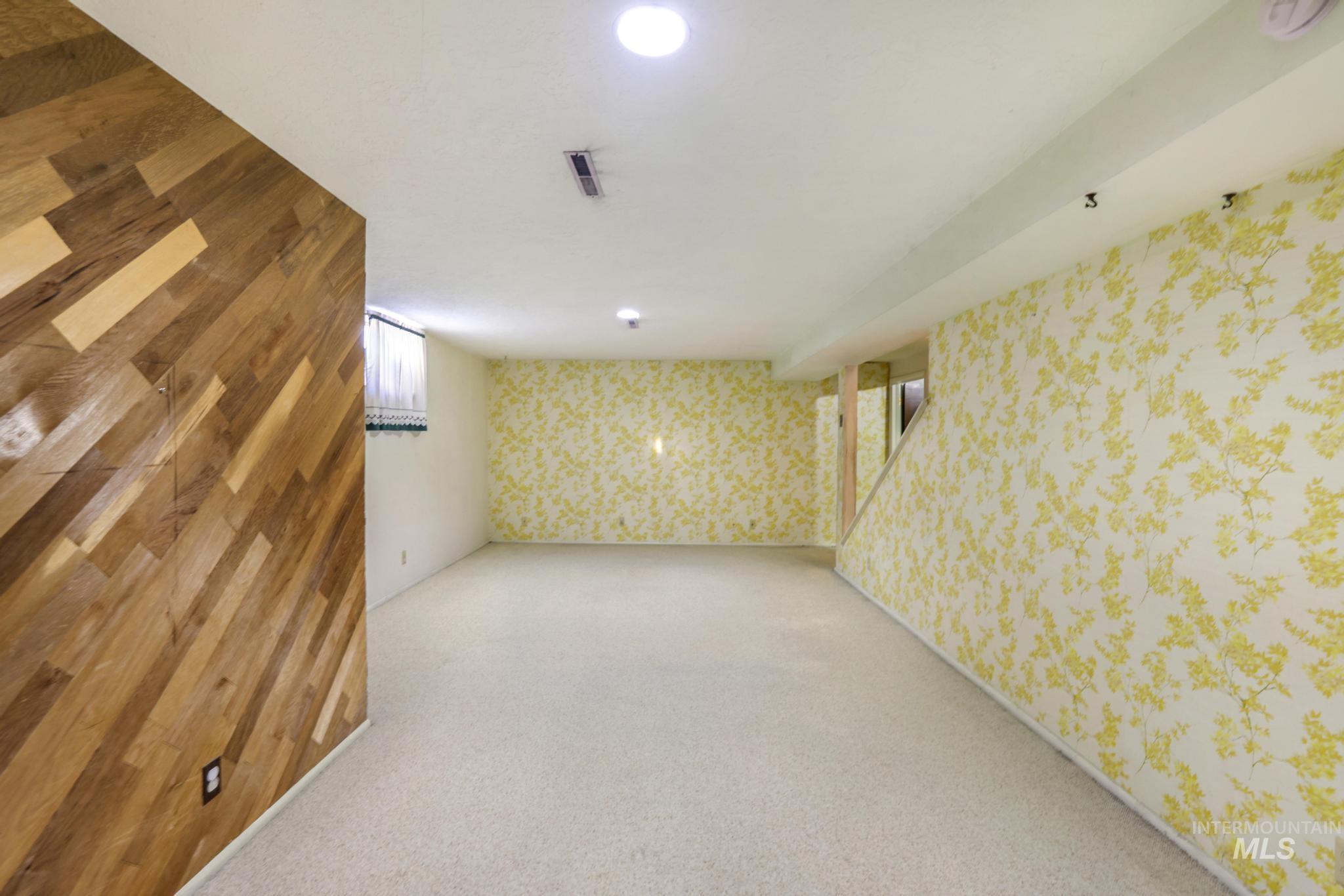 Finished below grade area featuring wallpapered walls, carpet flooring, and an accent wall