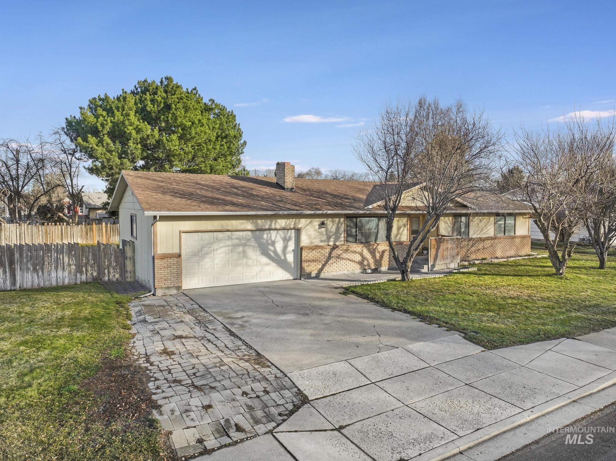 Ranch-style house featuring concrete driveway, brick siding, a chimney, and an attached garage