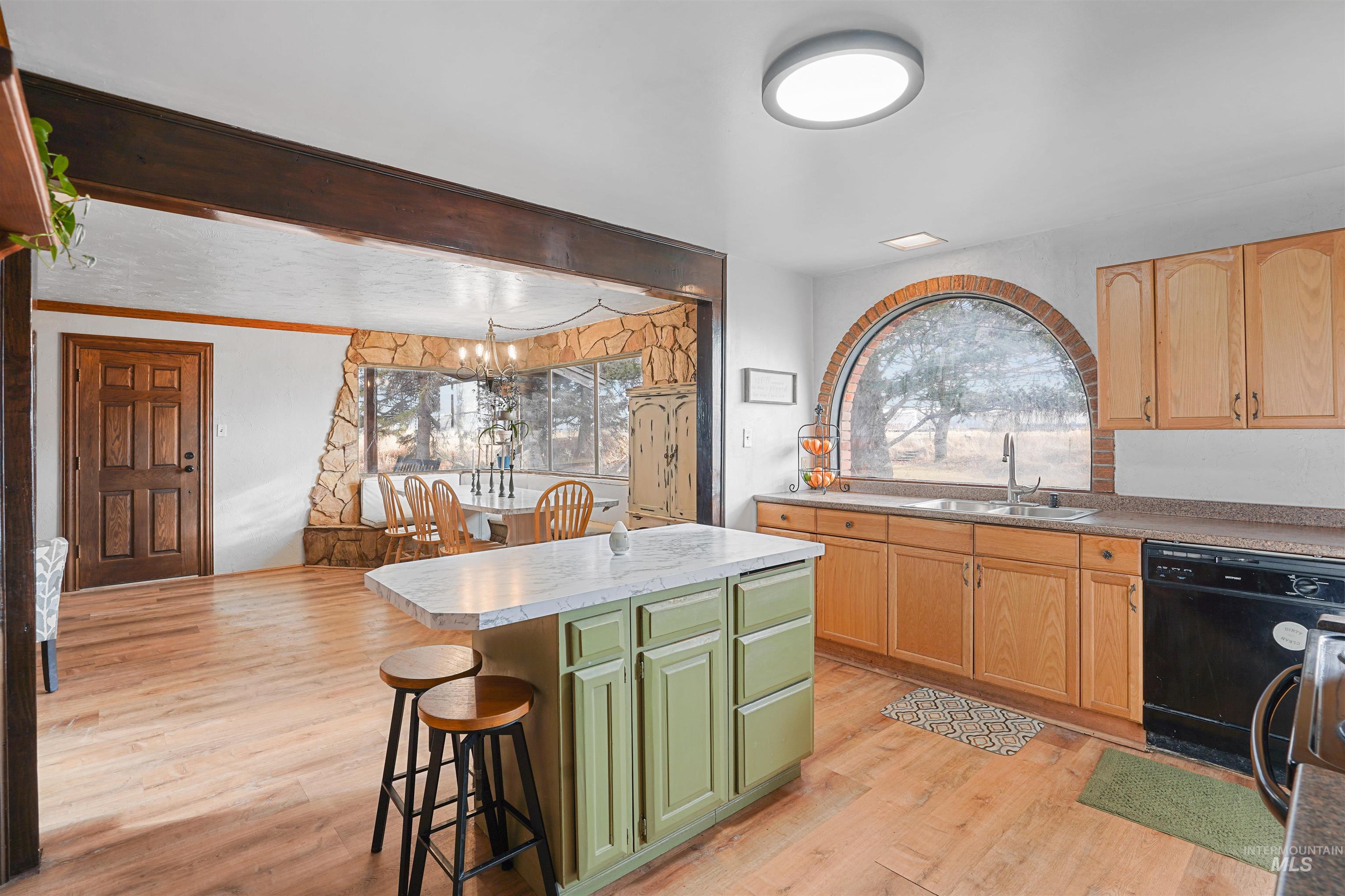 Kitchen featuring green cabinets, black dishwasher, light countertops, a kitchen bar, and a kitchen island