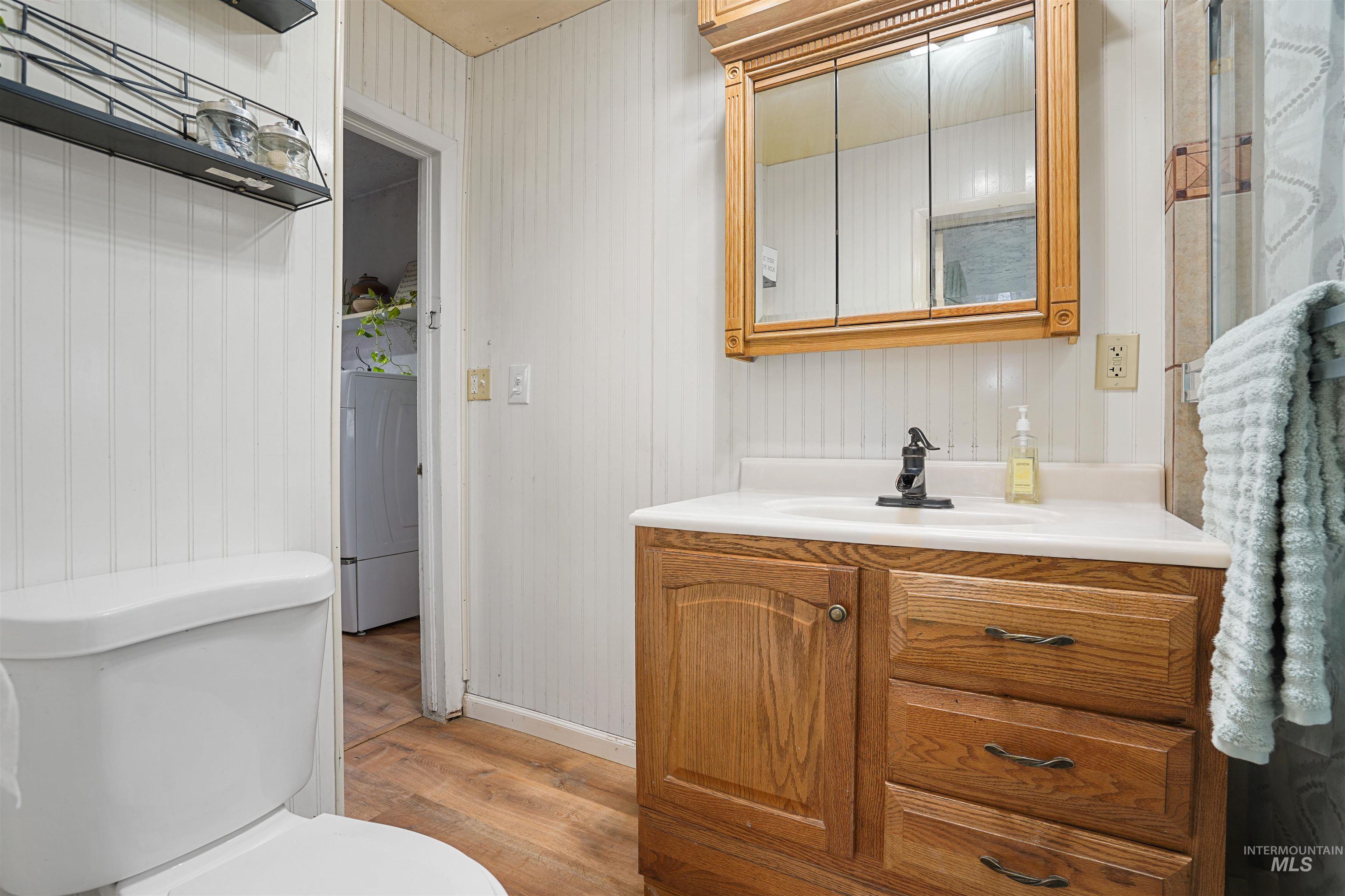Half bath featuring vanity, light wood-style floors, washer / clothes dryer, and wooden walls