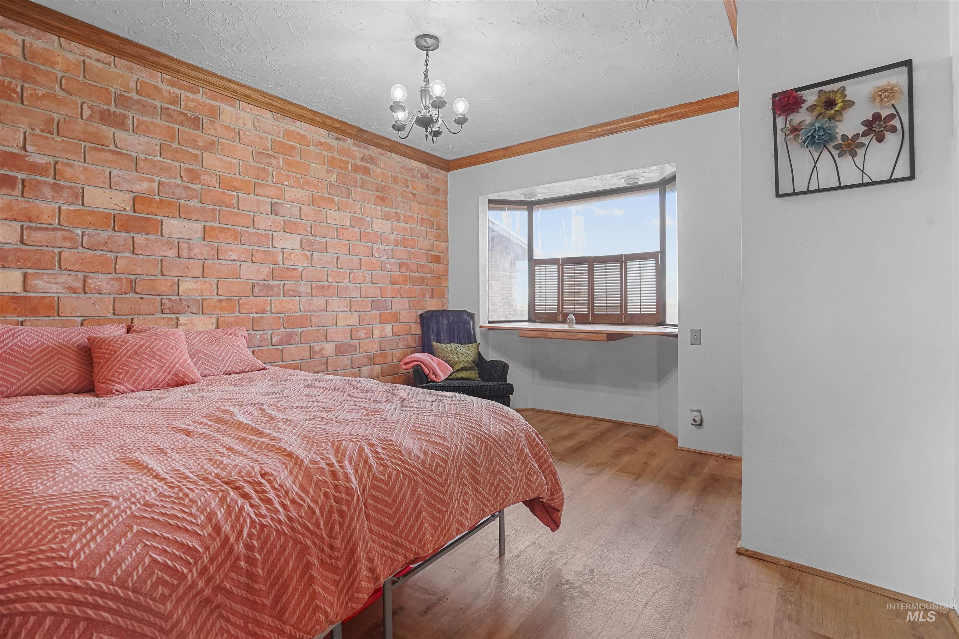Bedroom with brick wall, ornamental molding, light wood finished floors, a textured ceiling, and a chandelier