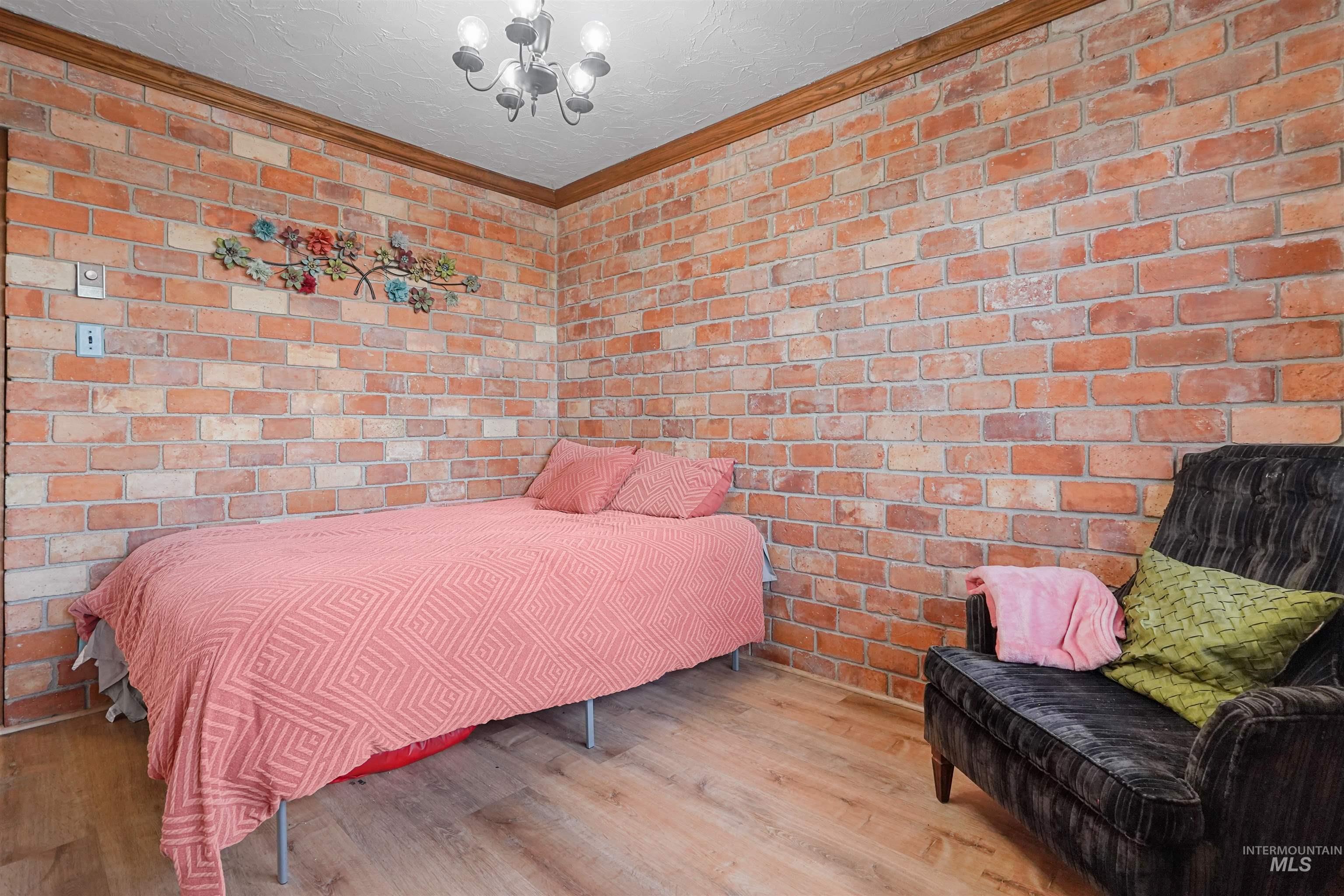 Bedroom featuring brick wall, wood finished floors, a chandelier, crown molding, and a textured ceiling