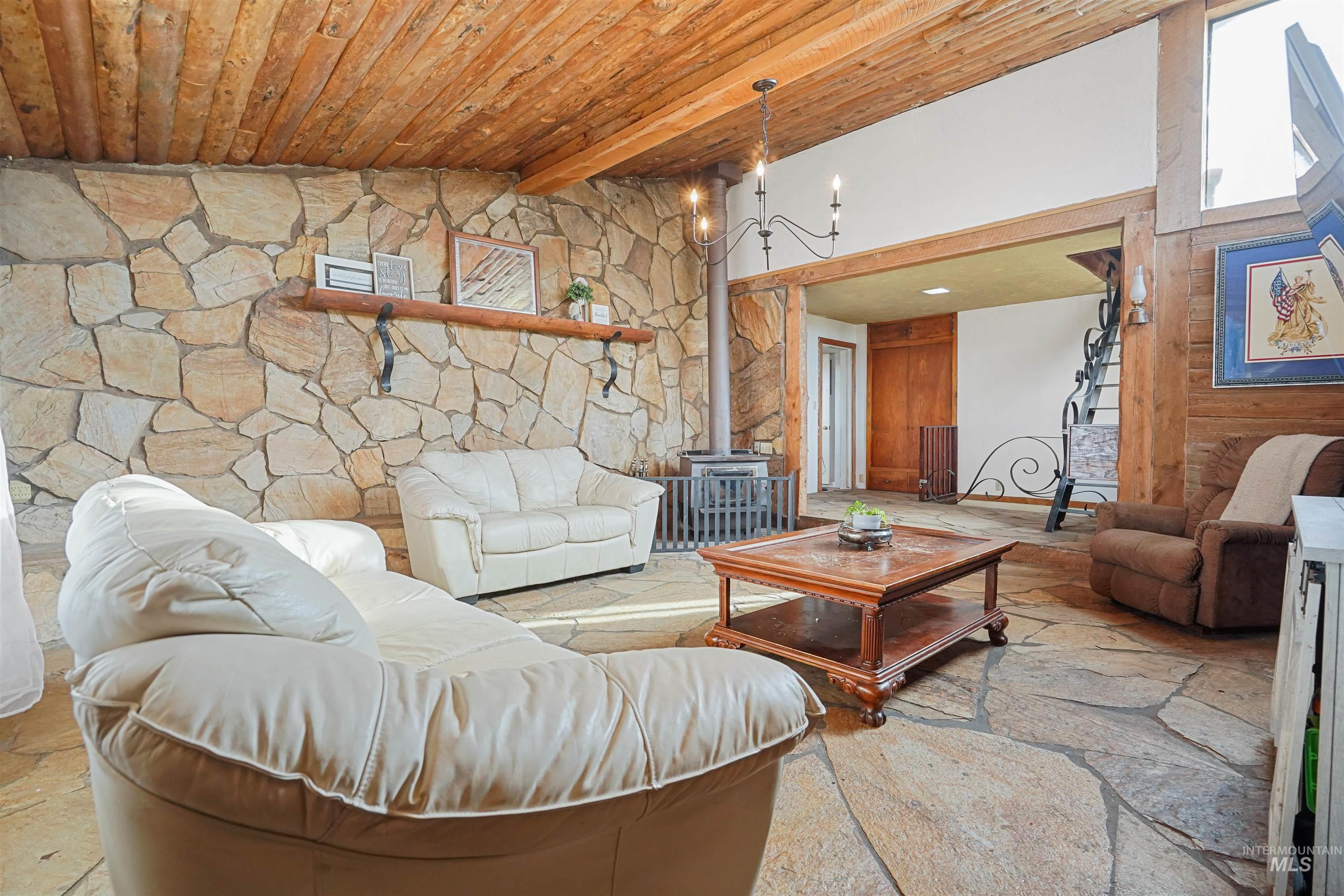 Living room featuring a wood stove, a wood ceiling with exposed beams, and a chandelier
