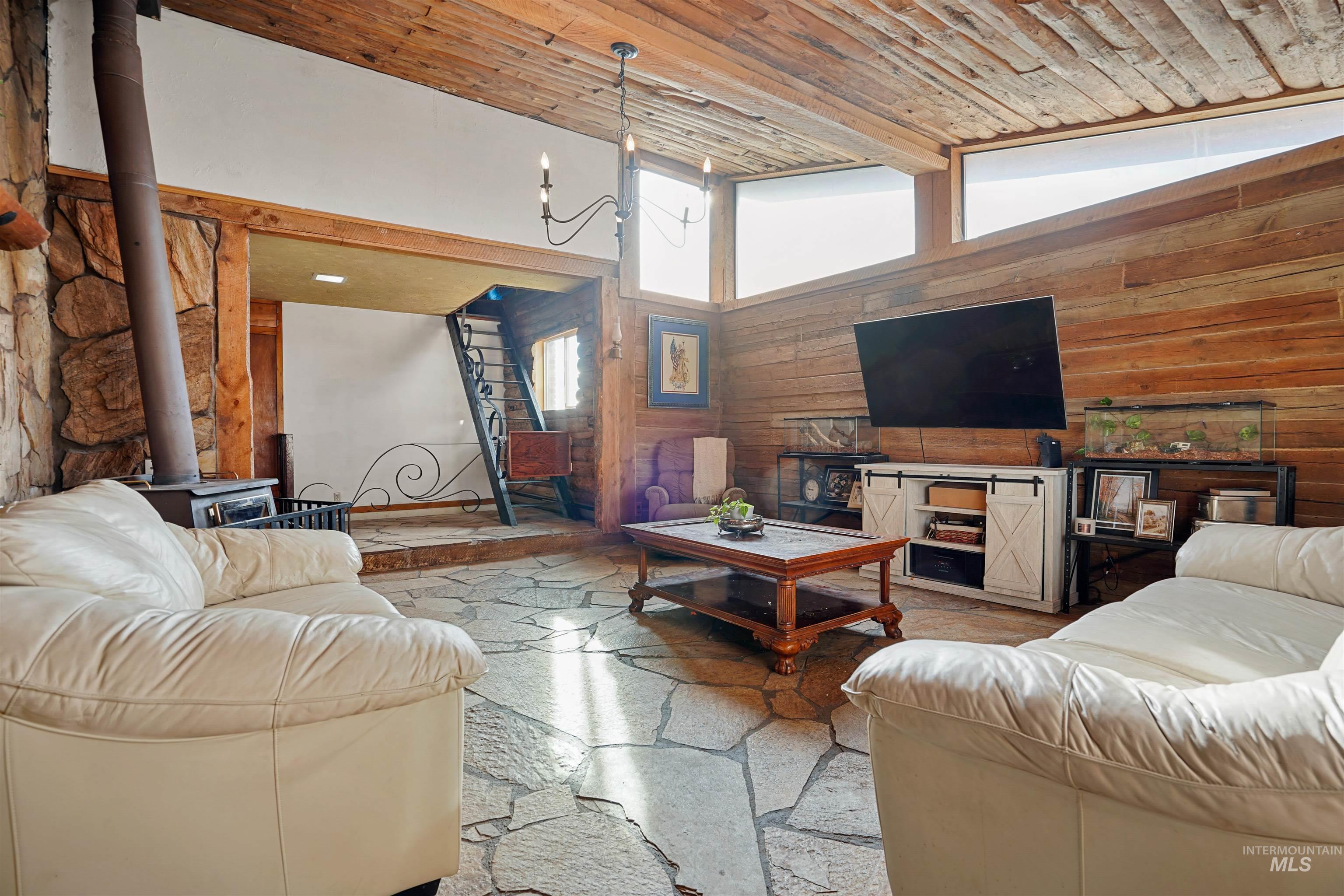 Living area with wood walls, wood ceiling, high vaulted ceiling, a wood stove, and a chandelier