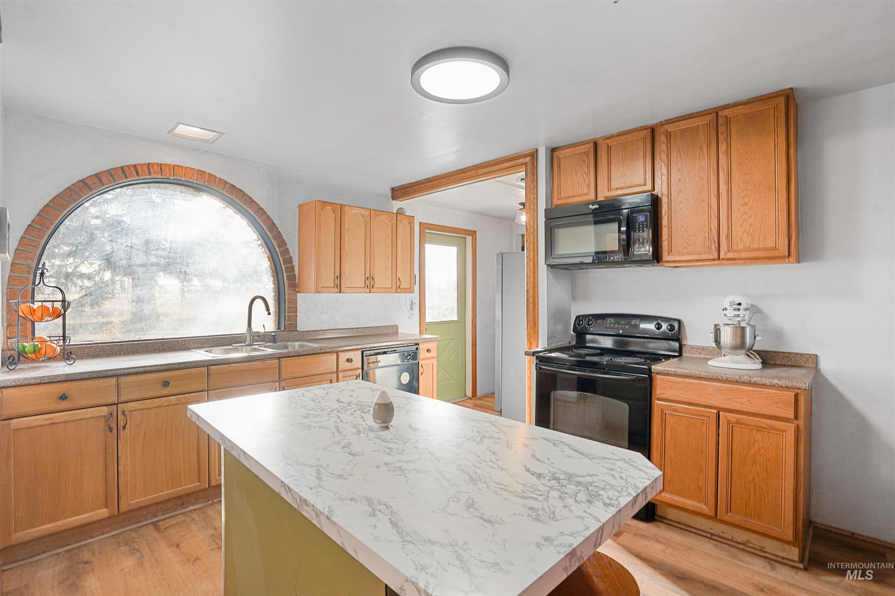 Kitchen featuring light countertops, black appliances, light wood-style flooring, and a kitchen island