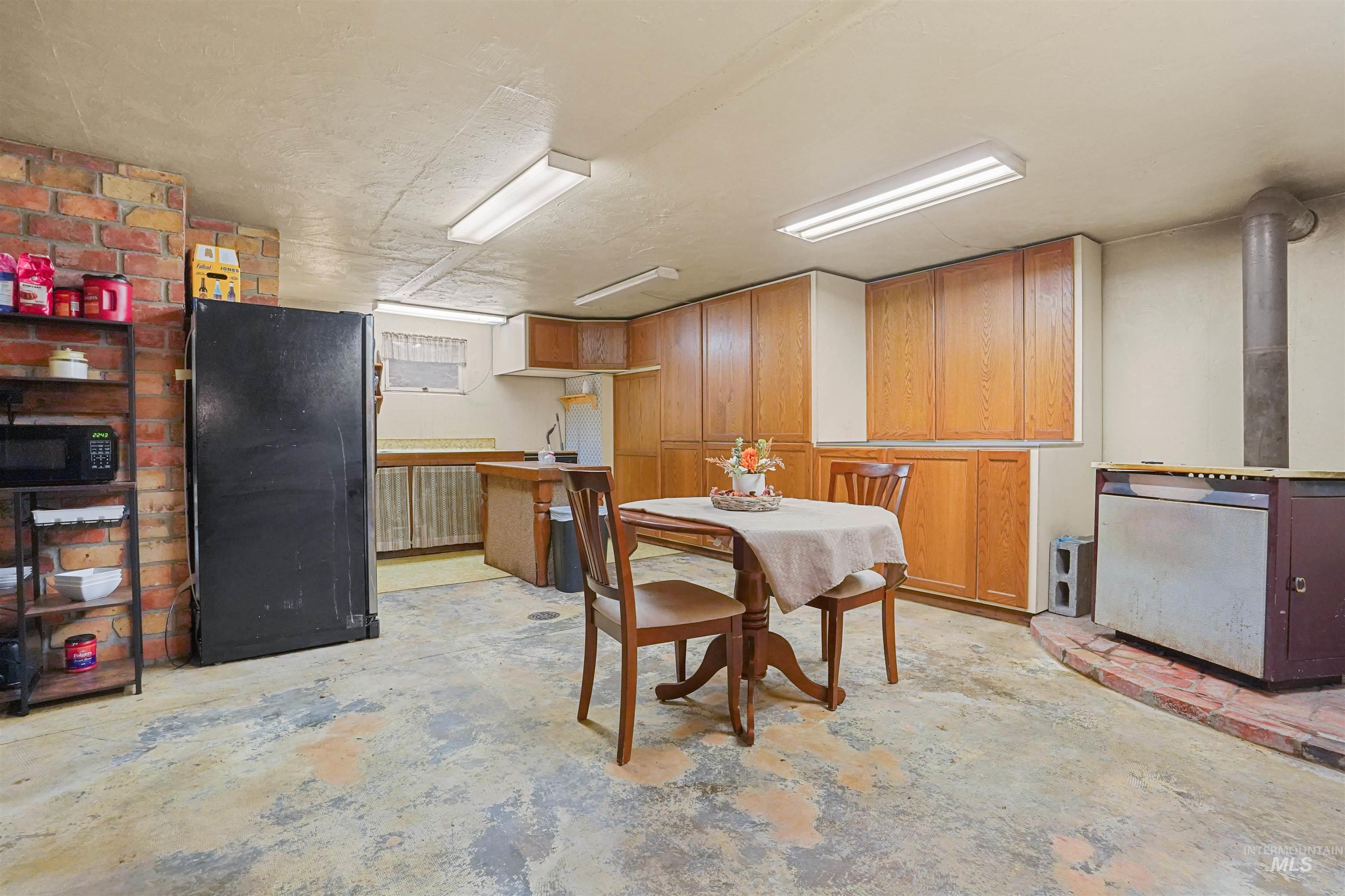 Kitchen featuring unfinished concrete flooring, black appliances, brown cabinetry, a wood stove, and light countertops