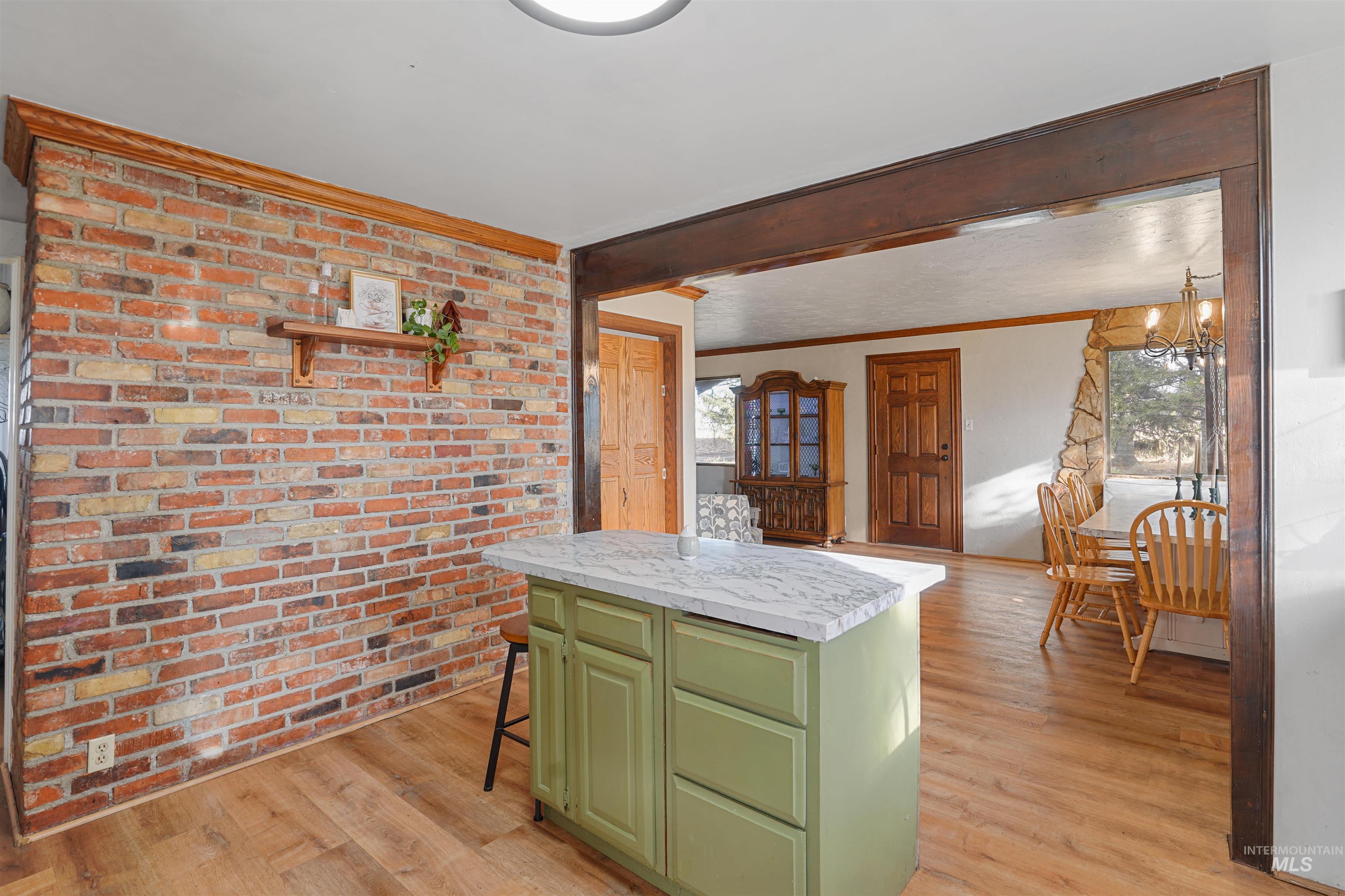 Kitchen with green cabinetry, brick wall, light wood-type flooring, a kitchen breakfast bar, and a kitchen island