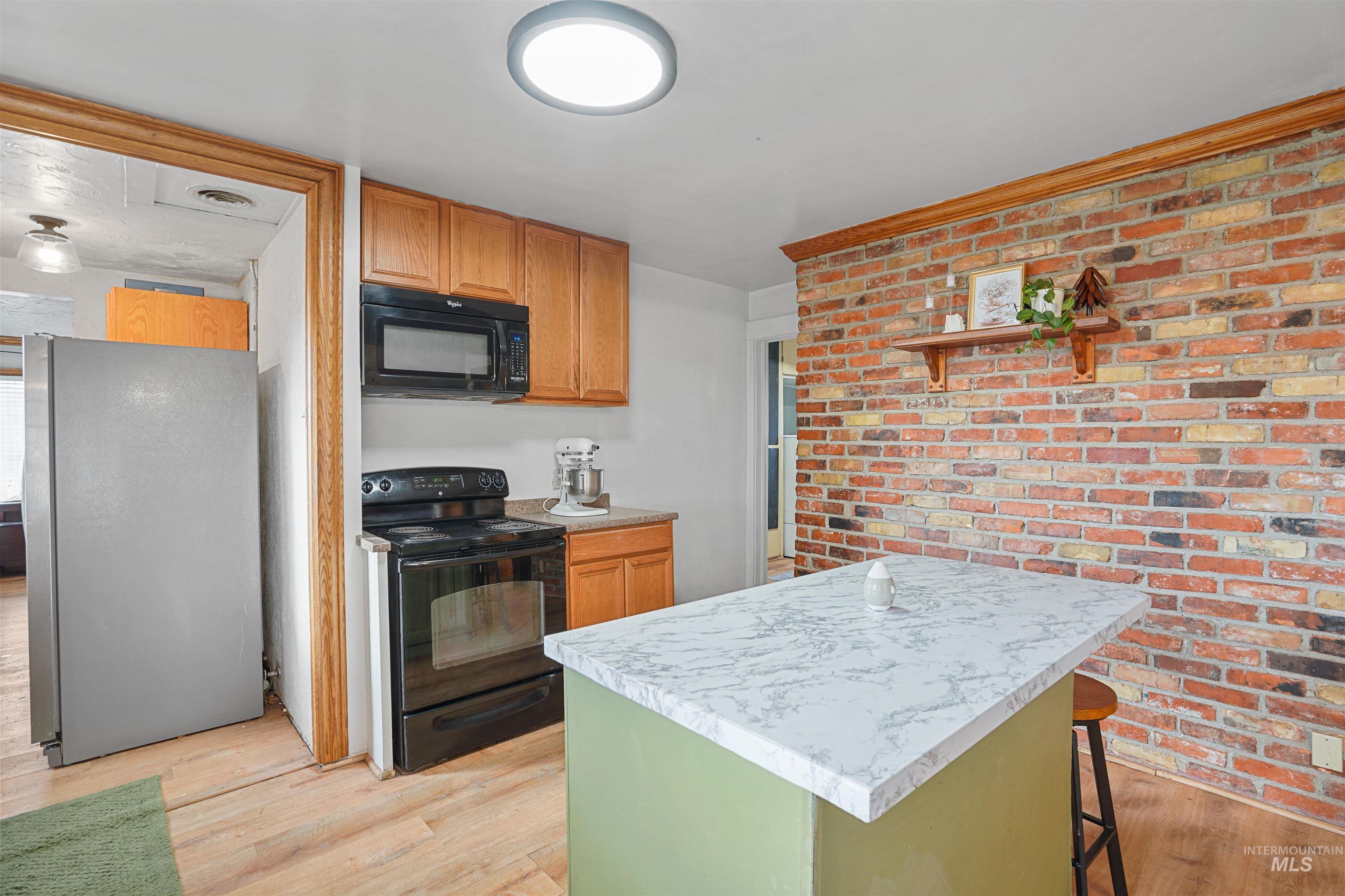 Kitchen with black appliances, light countertops, brown cabinetry, light wood-style floors, and brick wall