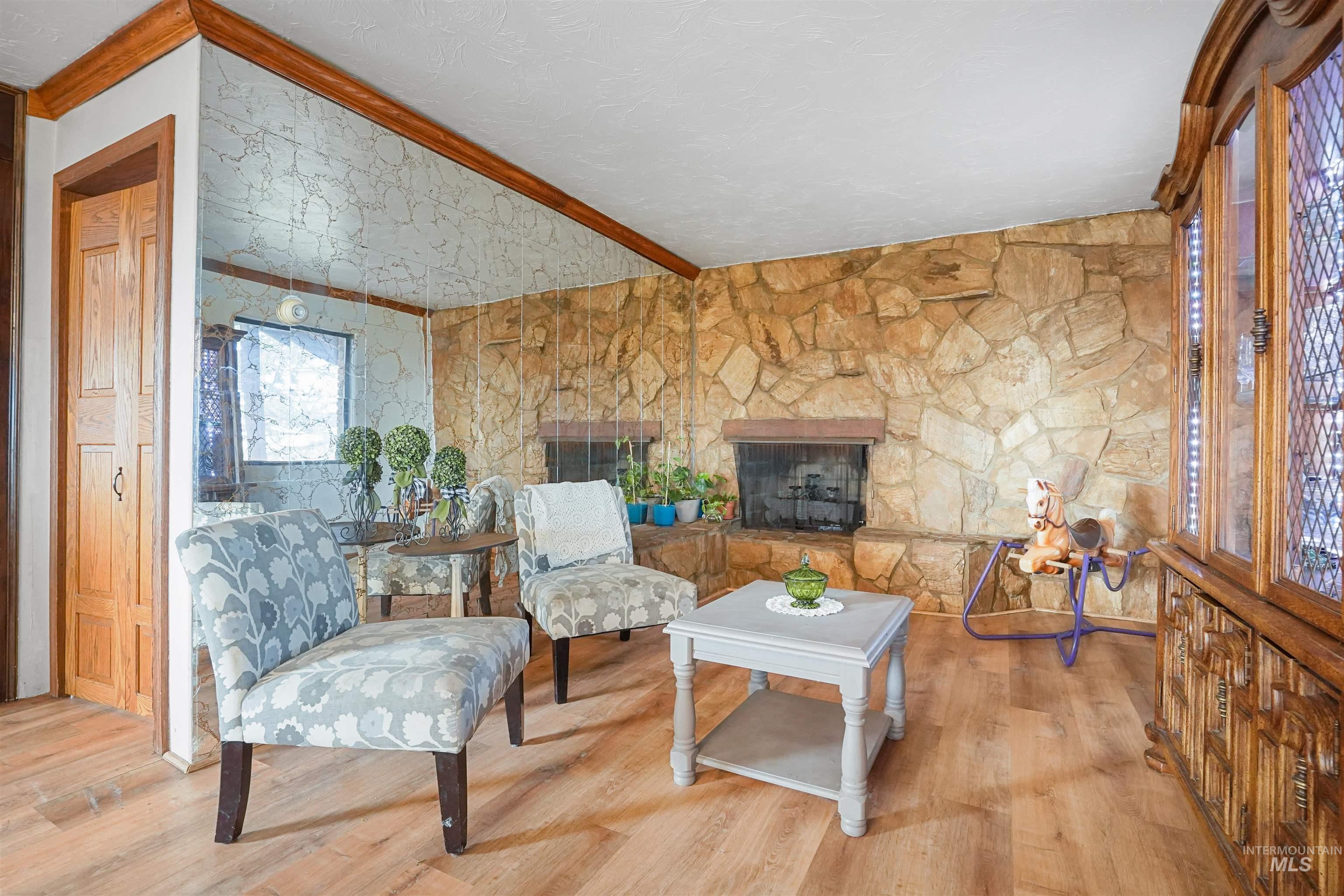 Sitting room with wood finished floors, a stone fireplace, and ornamental molding