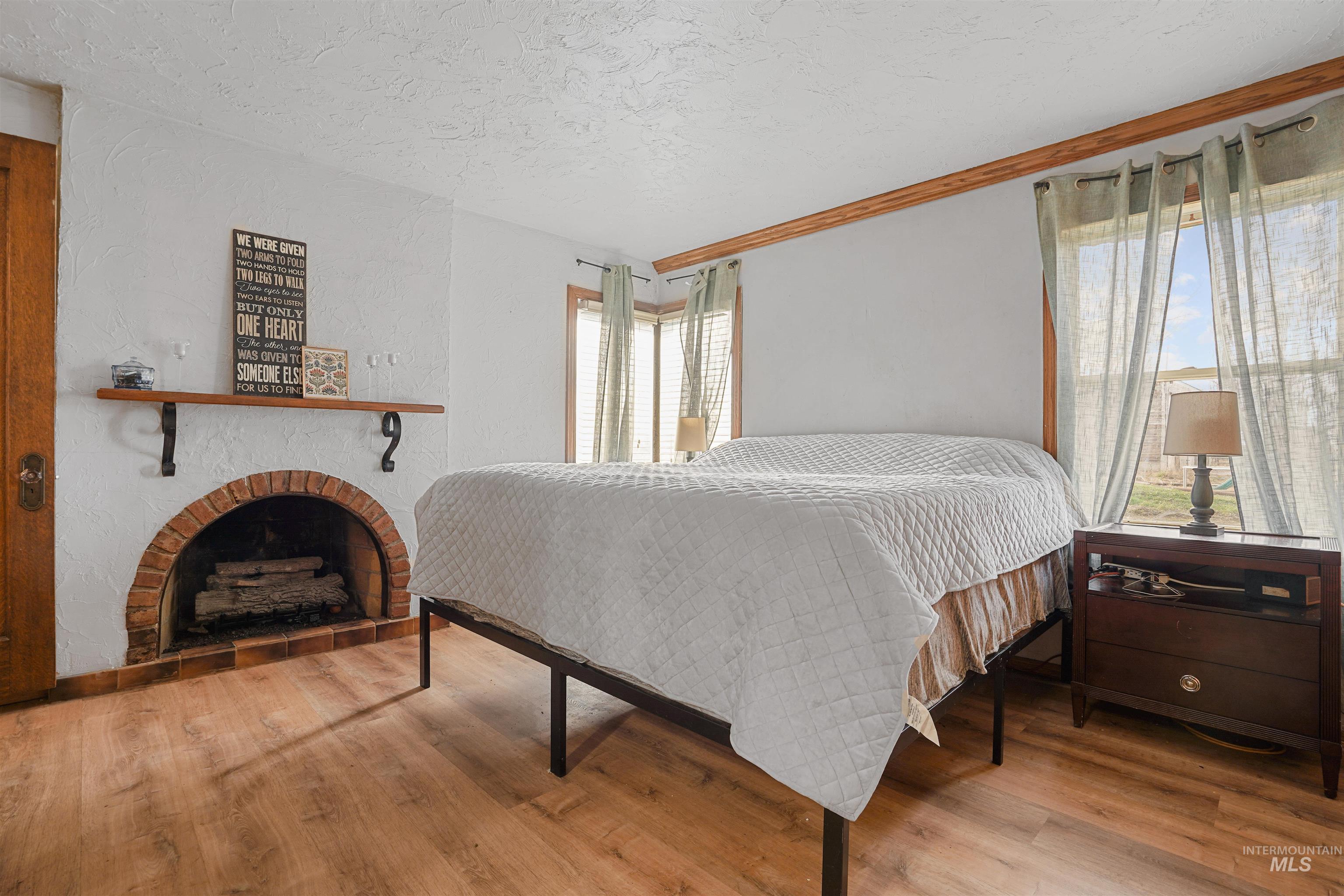 Bedroom with a brick fireplace, a textured ceiling, and wood finished floors