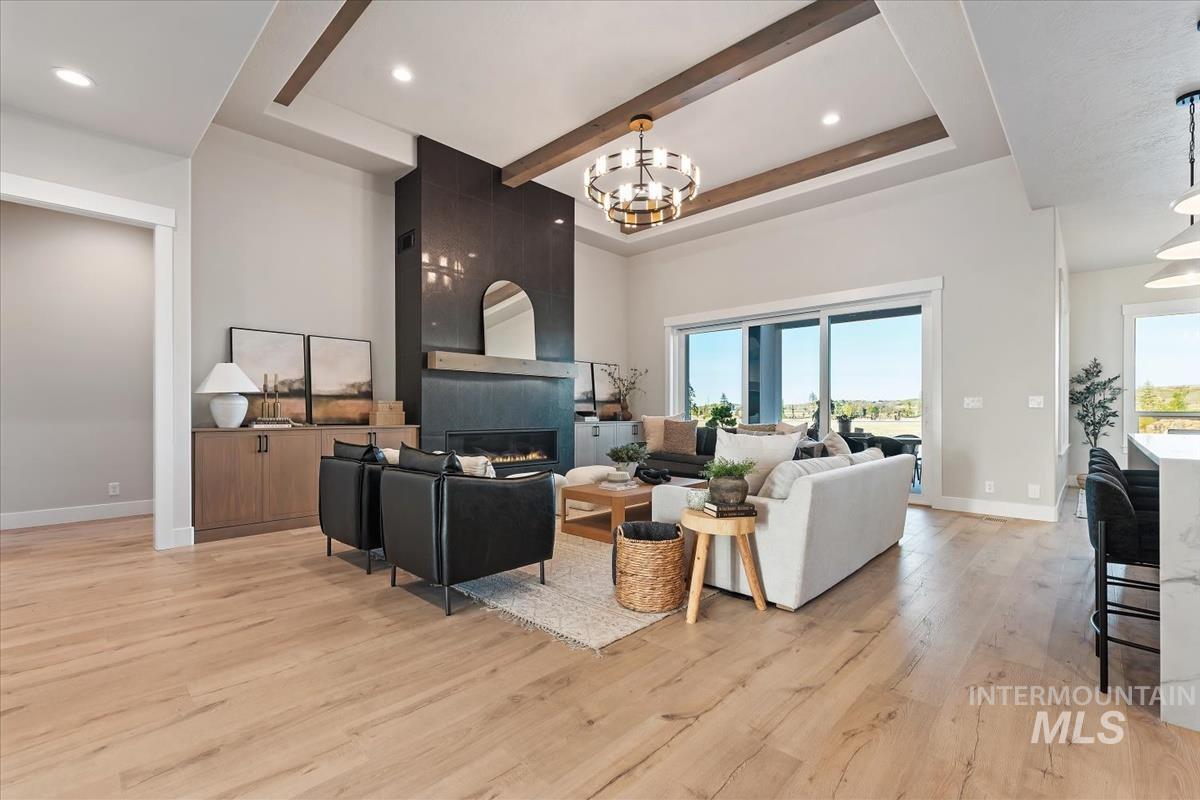 Living room with a chandelier, a fireplace, light wood finished floors, recessed lighting, and beam ceiling