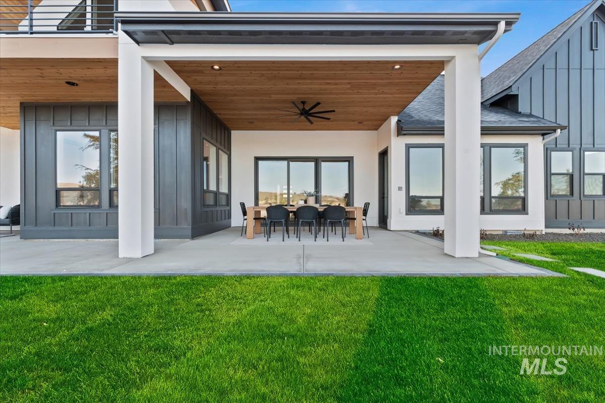 Back of house with ceiling fan, board and batten siding, a patio area, and a yard
