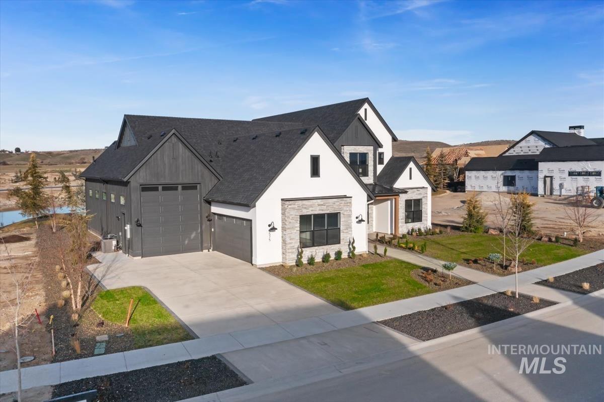 Modern farmhouse with stone siding, driveway, a front lawn, and roof with shingles