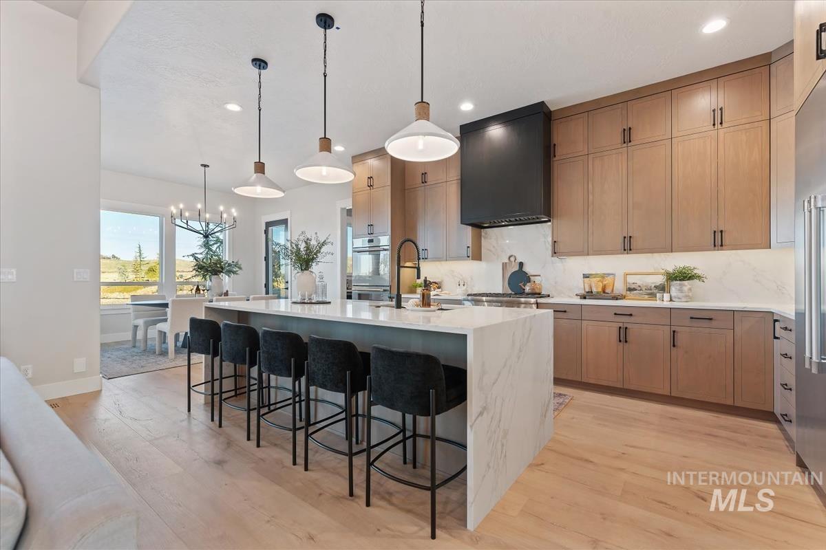 Kitchen featuring decorative light fixtures, light stone counters, light wood-style floors, a spacious island, and a breakfast bar