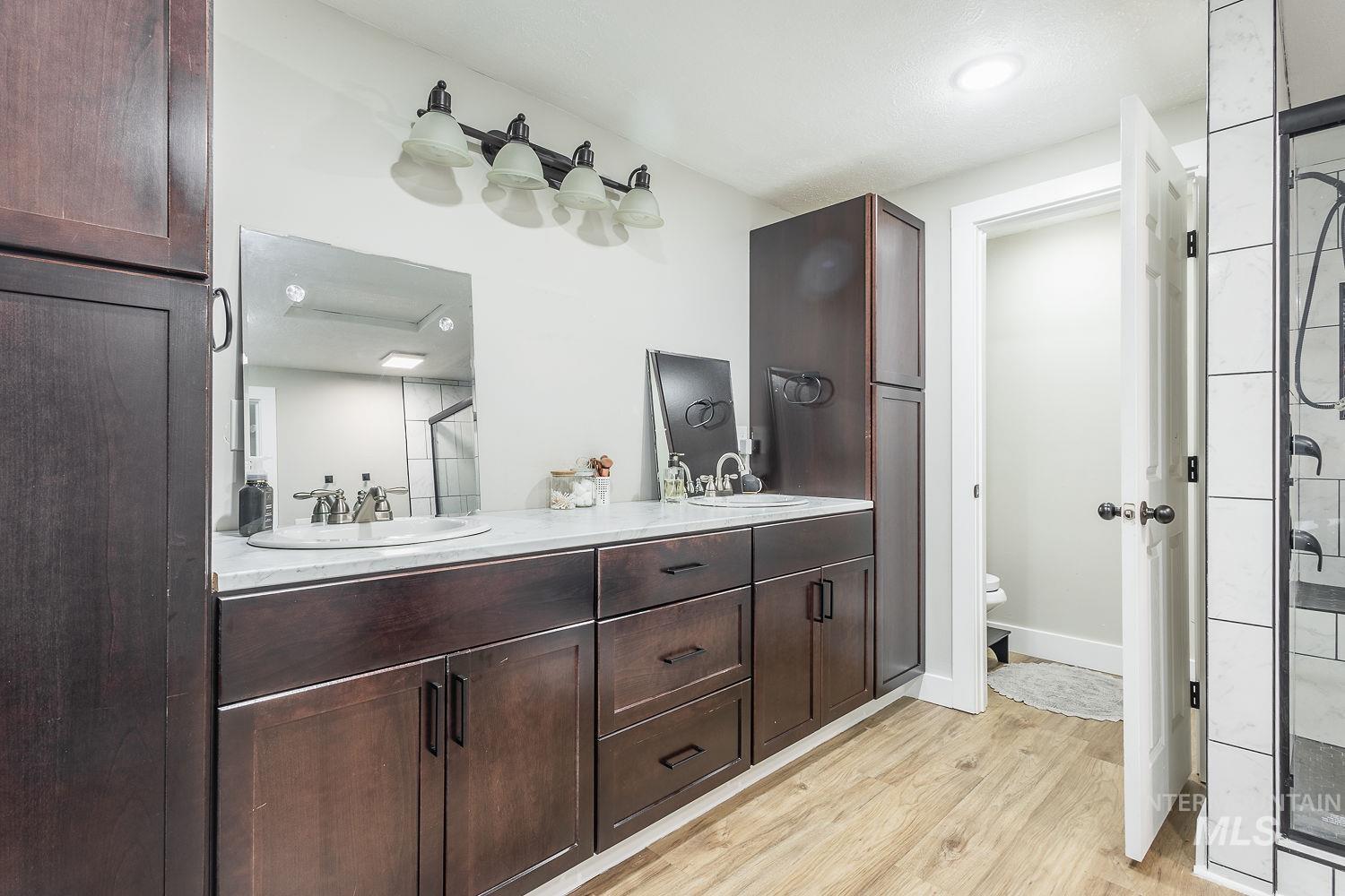 Bathroom with double vanity, a stall shower, and light wood-type flooring