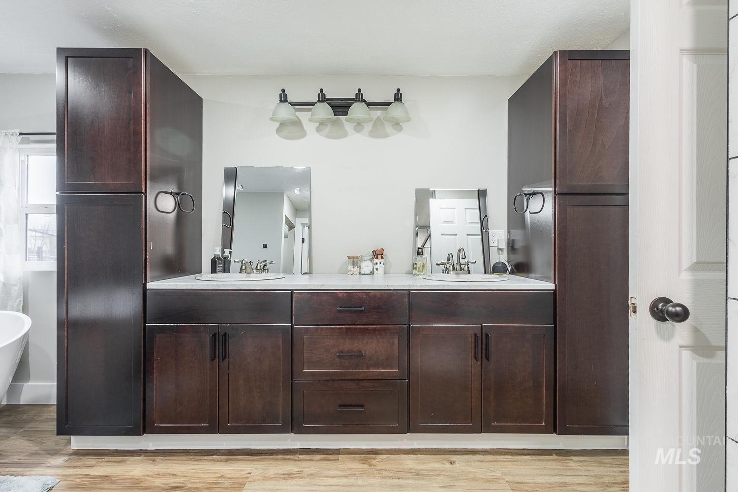 Full bathroom with double vanity, light wood finished floors, and a soaking tub