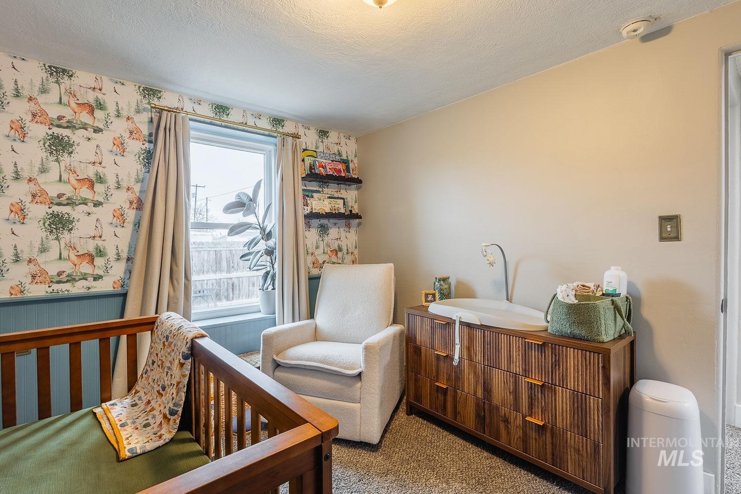 Carpeted bedroom with a crib, a textured ceiling, and wallpapered walls