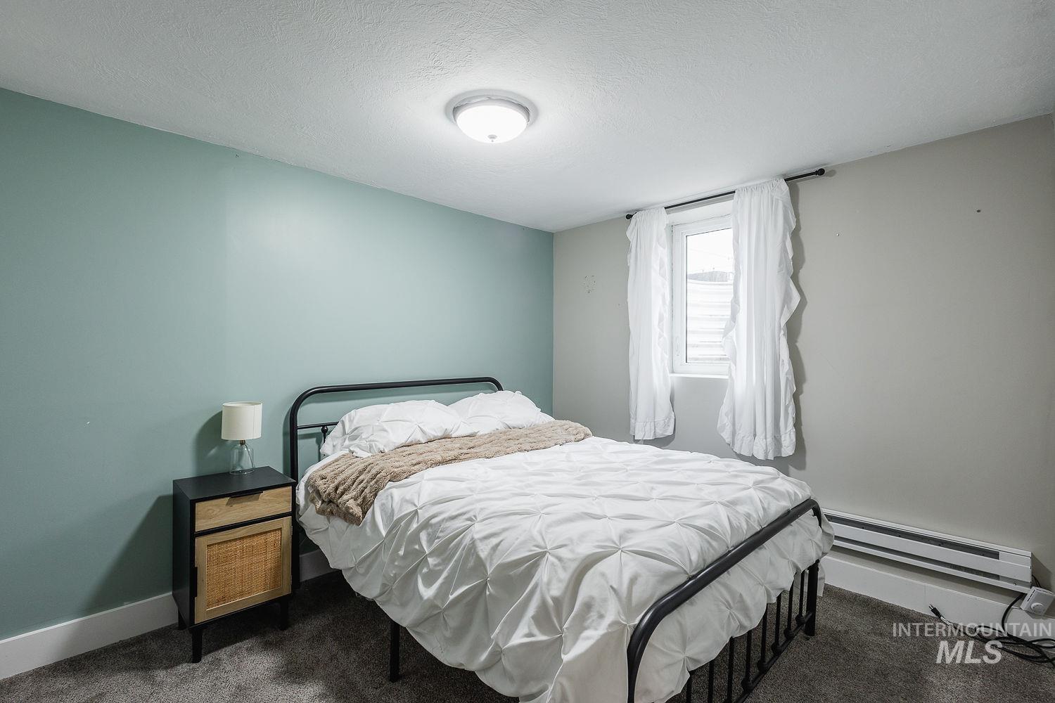 Carpeted bedroom with a textured ceiling and a baseboard heating unit