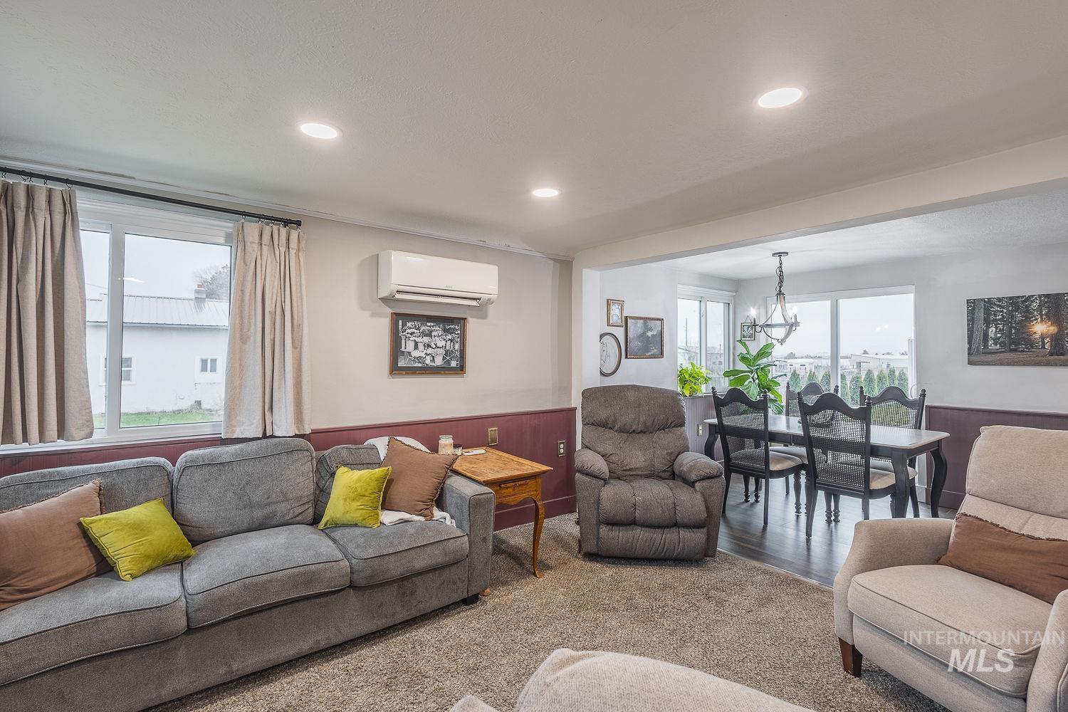 Living room with a chandelier, a wainscoted wall, carpet, a wall mounted air conditioner, and recessed lighting