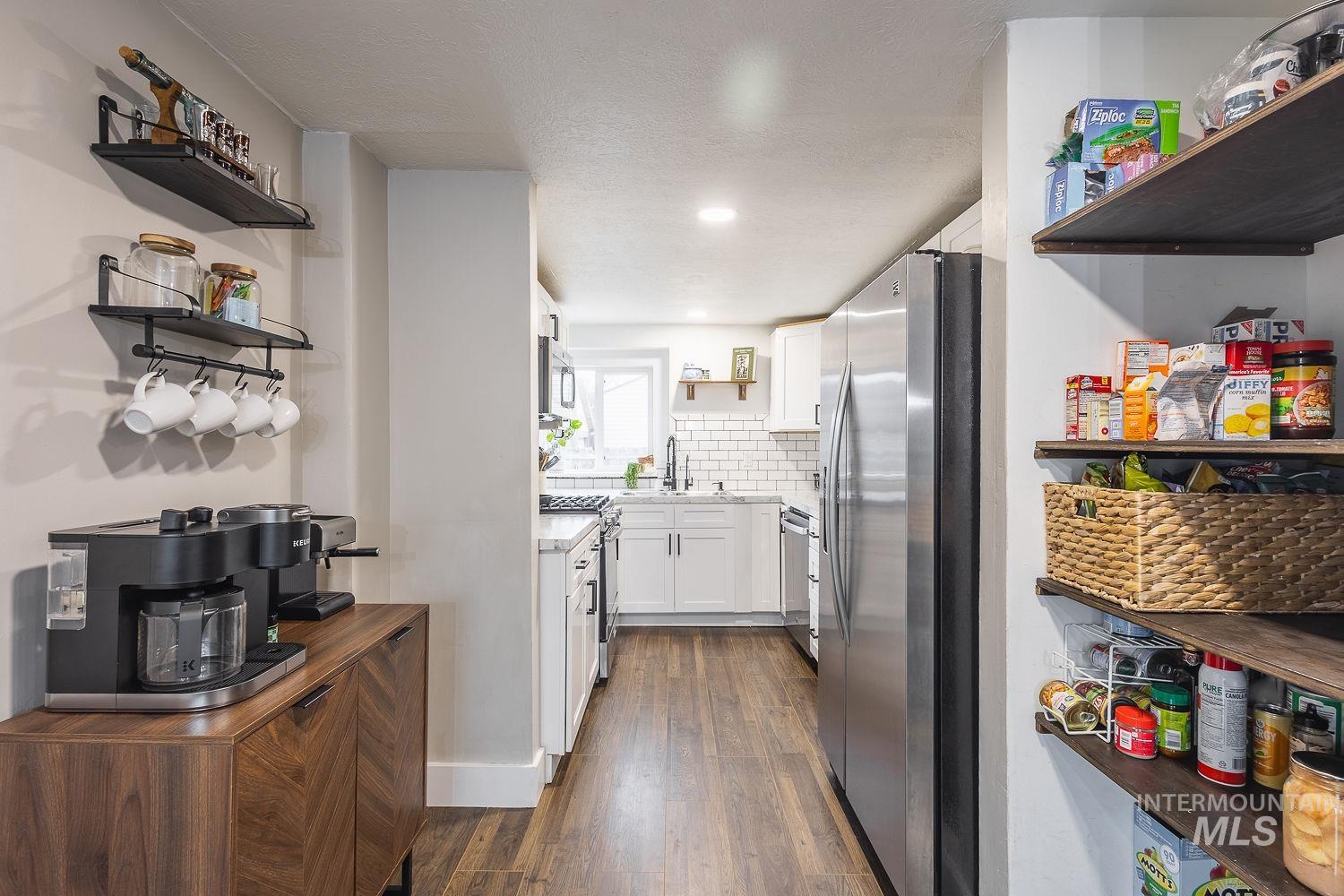 Kitchen with open shelves, white cabinetry, stainless steel appliances, dark wood-style floors, and backsplash