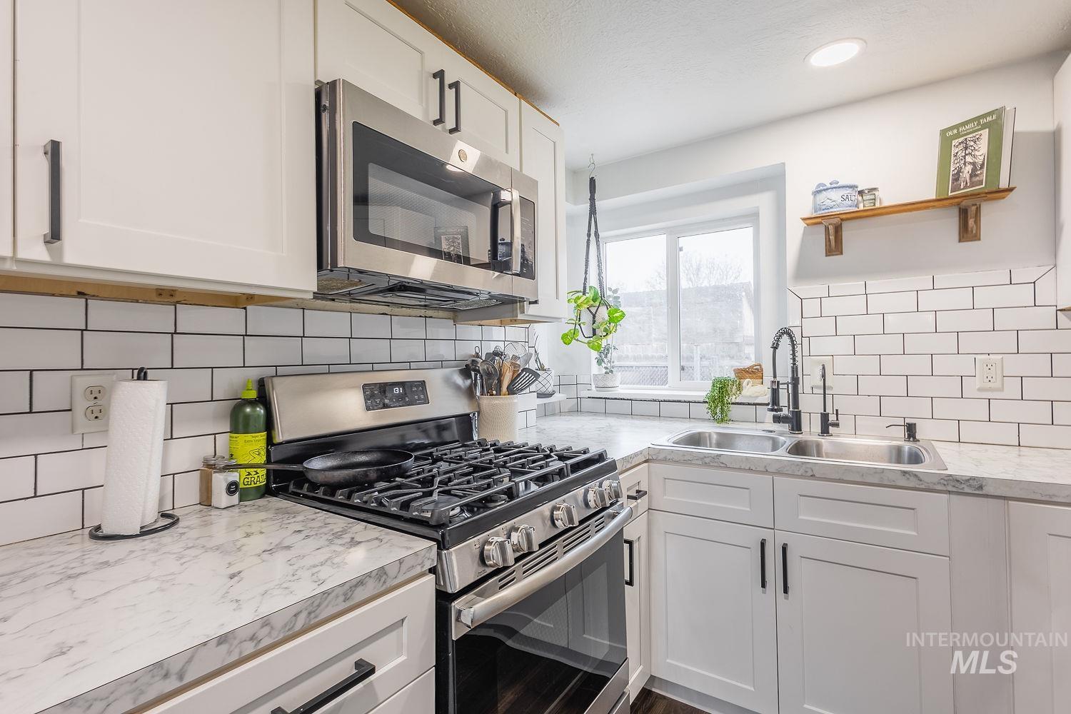 Kitchen with stainless steel appliances, white cabinetry, open shelves, tasteful backsplash, and light countertops