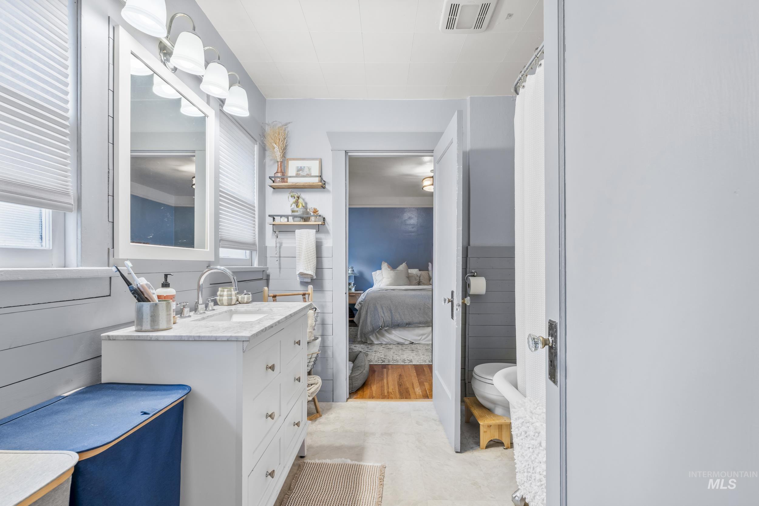 Ensuite bathroom featuring vanity, a shower with curtain, and a wainscoted wall