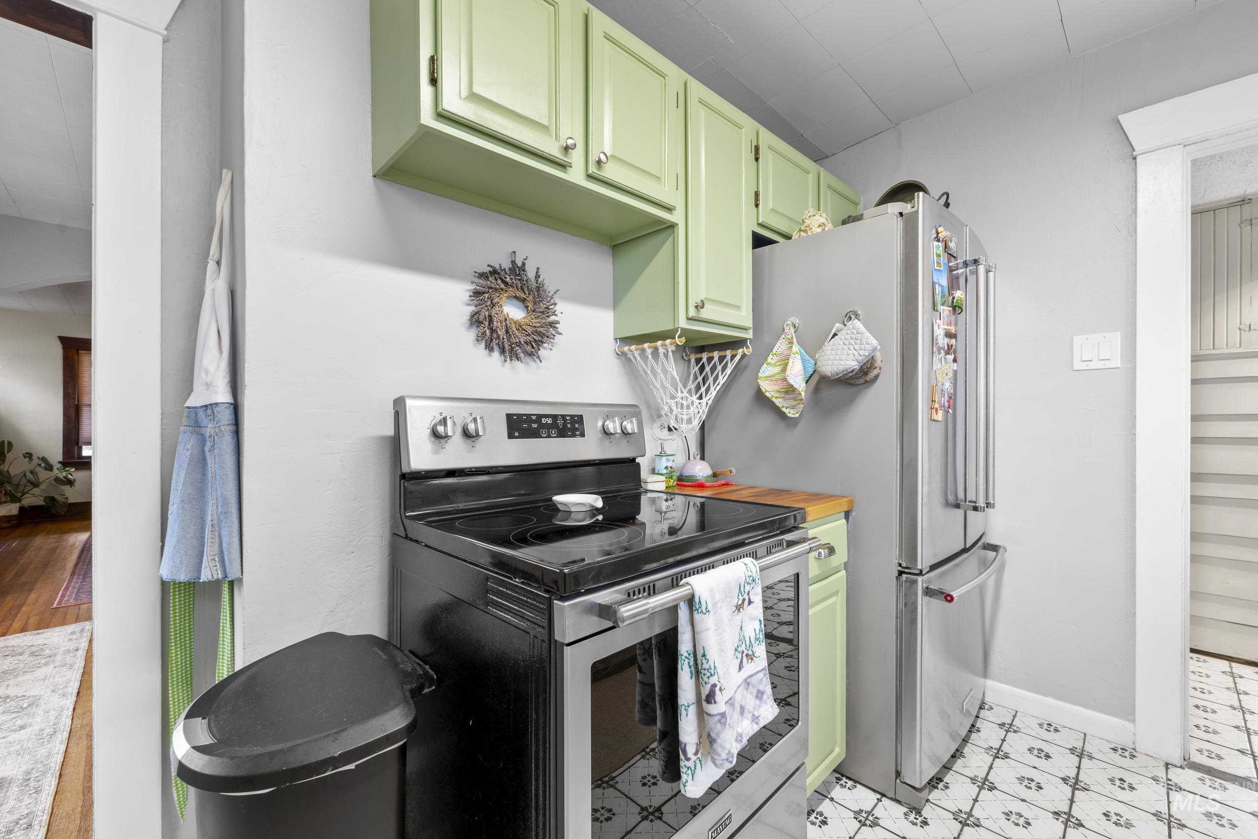 Kitchen with appliances with stainless steel finishes, green cabinets, light floors, and butcher block counters